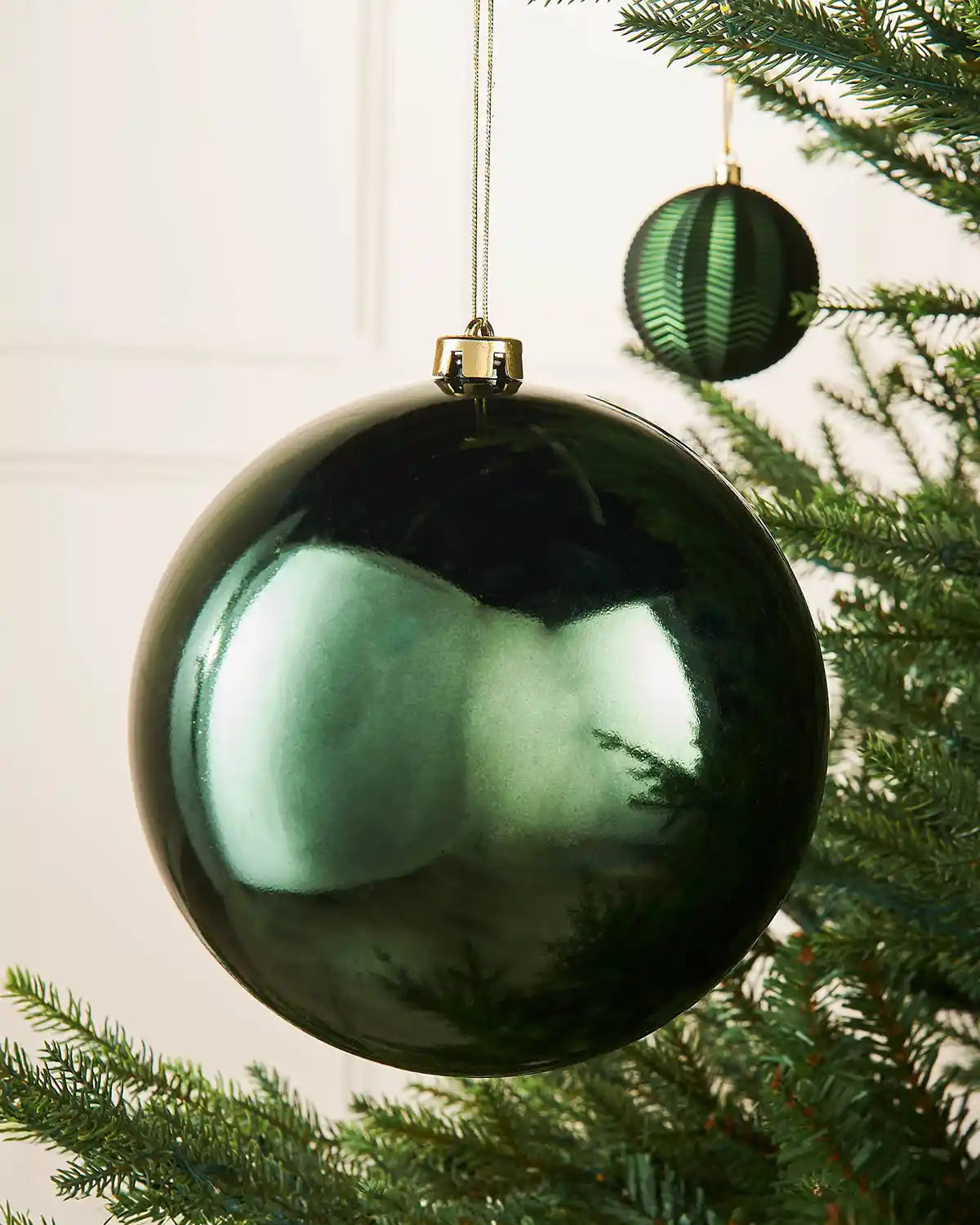 Oversized gloss green bauble on a Christmas tree branch with a smaller green bauble