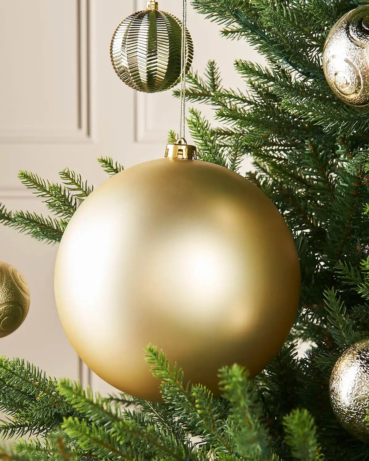 Oversized gold matt bauble on a Christmas tree branch with 4 smaller gold baubles in the background
