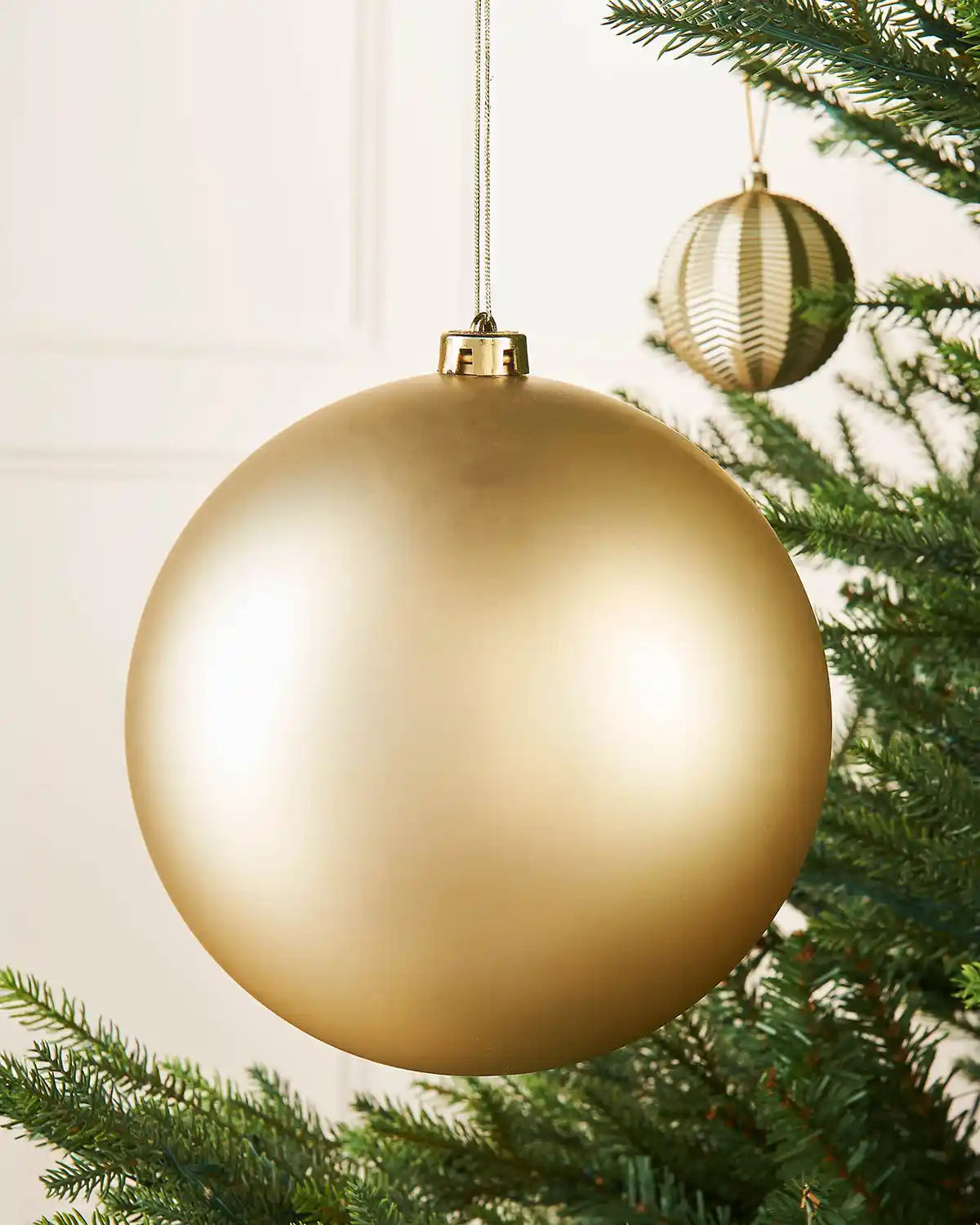 Oversized gold matt bauble on a Christmas tree branch with a smaller gold bauble in the background