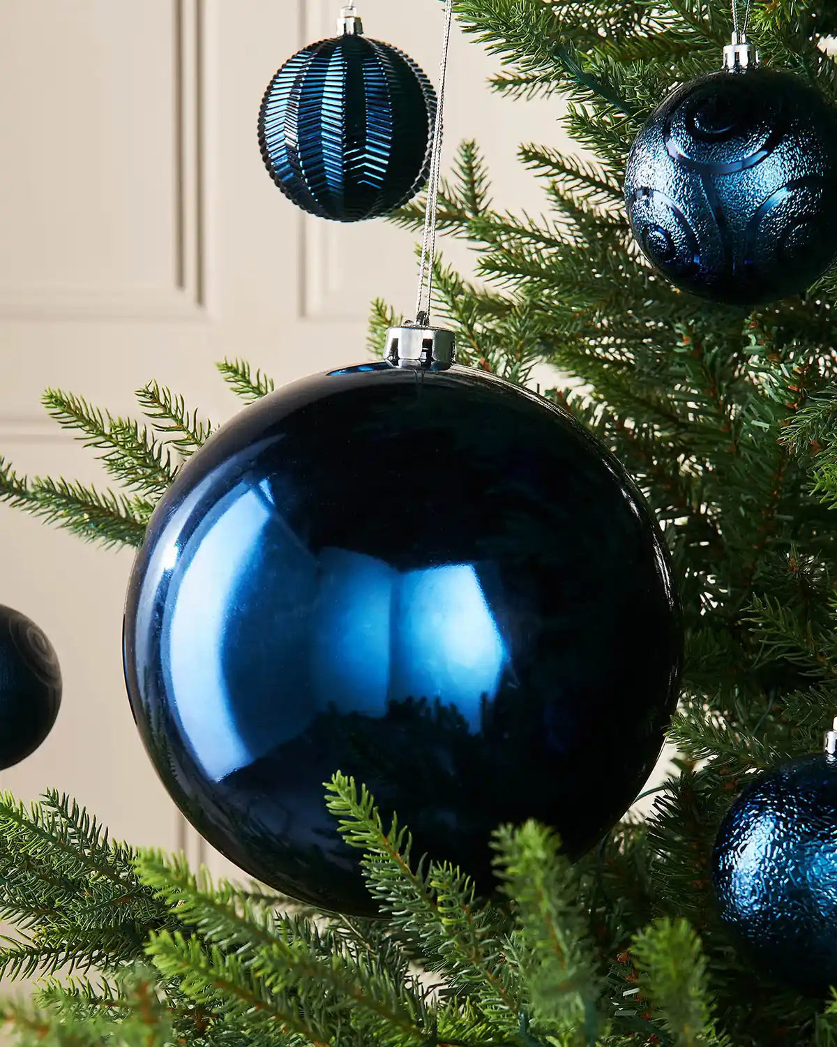 Oversized navy blue gloss bauble on a Christmas tree branch with 4 smaller Blue baubles in the background