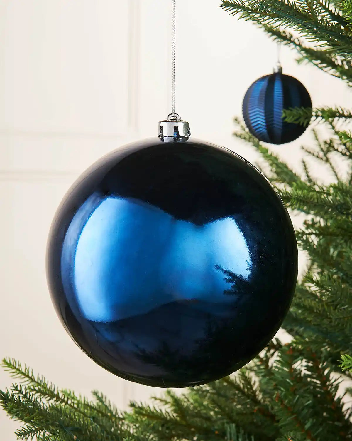 Oversized navy blue gloss bauble on a Christmas tree branch with a smaller Blue bauble in the background