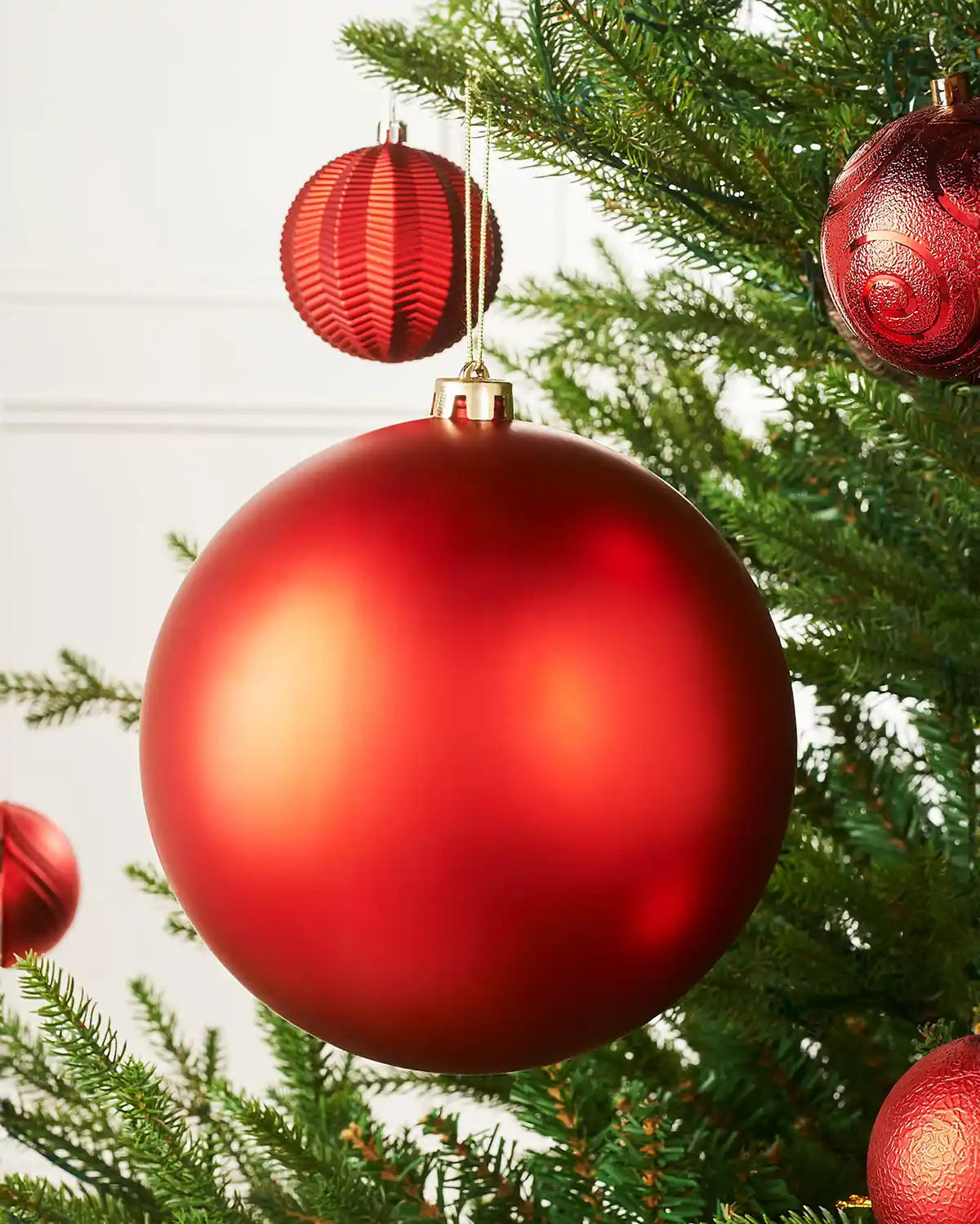 Oversized red matt bauble on a Christmas tree branch with 4 smaller red baubles in the background