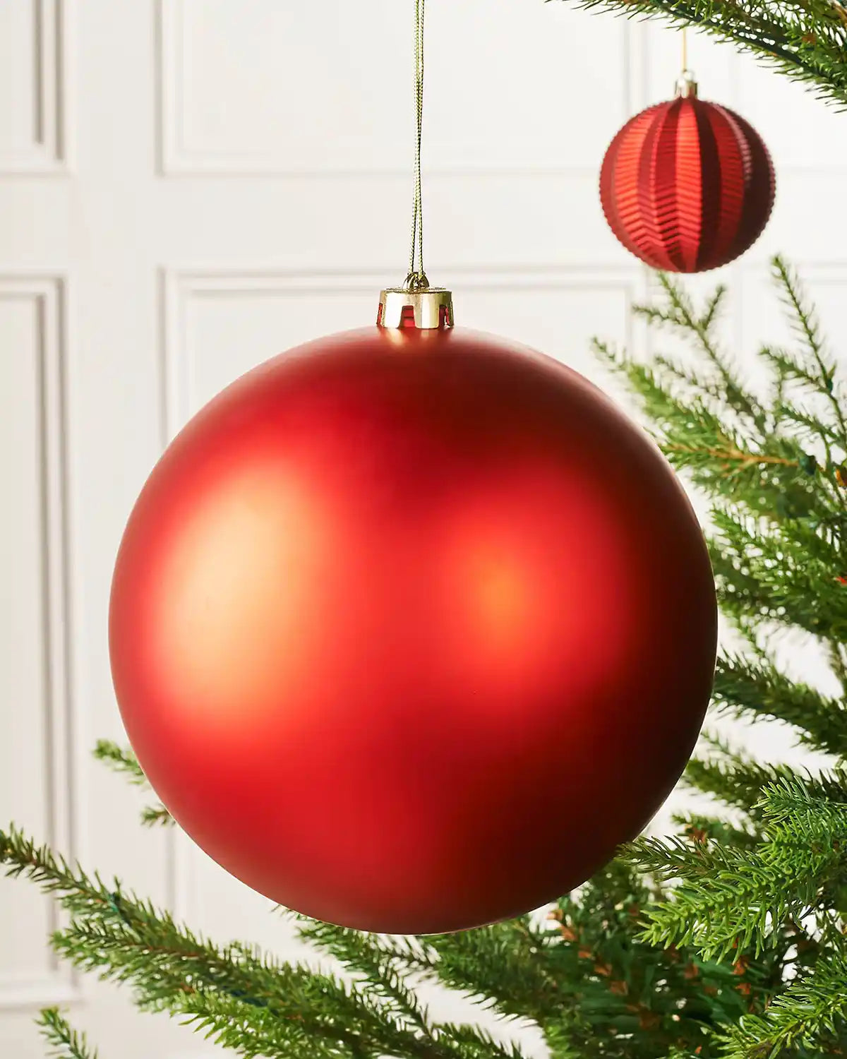 Oversized red matt bauble on a Christmas tree branch with a smaller red bauble in the background