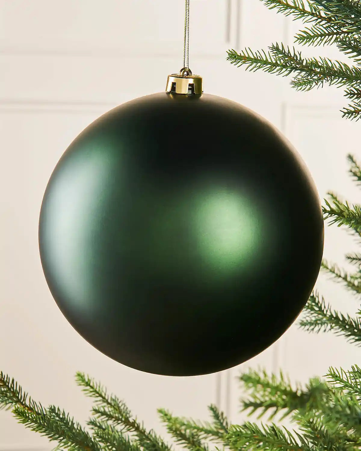 Oversized sage green bauble on a Christmas tree branch