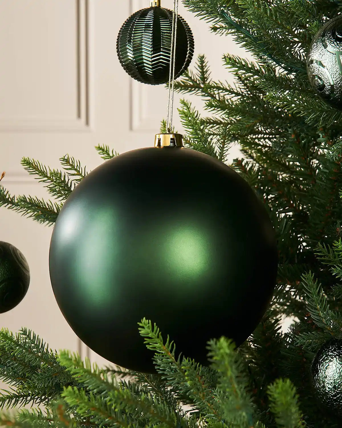 Oversized sage green bauble on a Christmas tree branch with 4 smaller sage green baubles in the background 