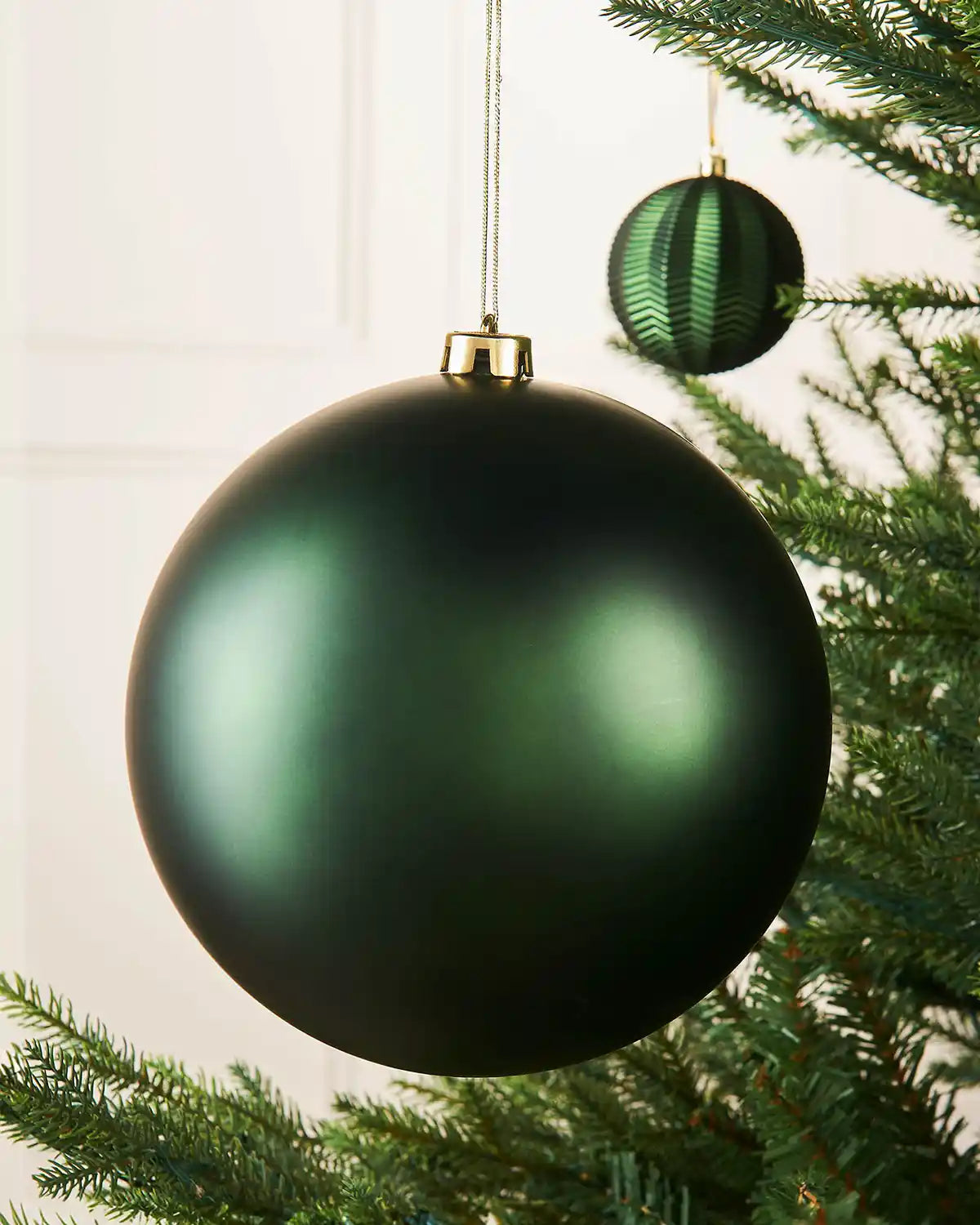Oversized sage green bauble on a Christmas tree branch with a smaller sage green bauble in the background