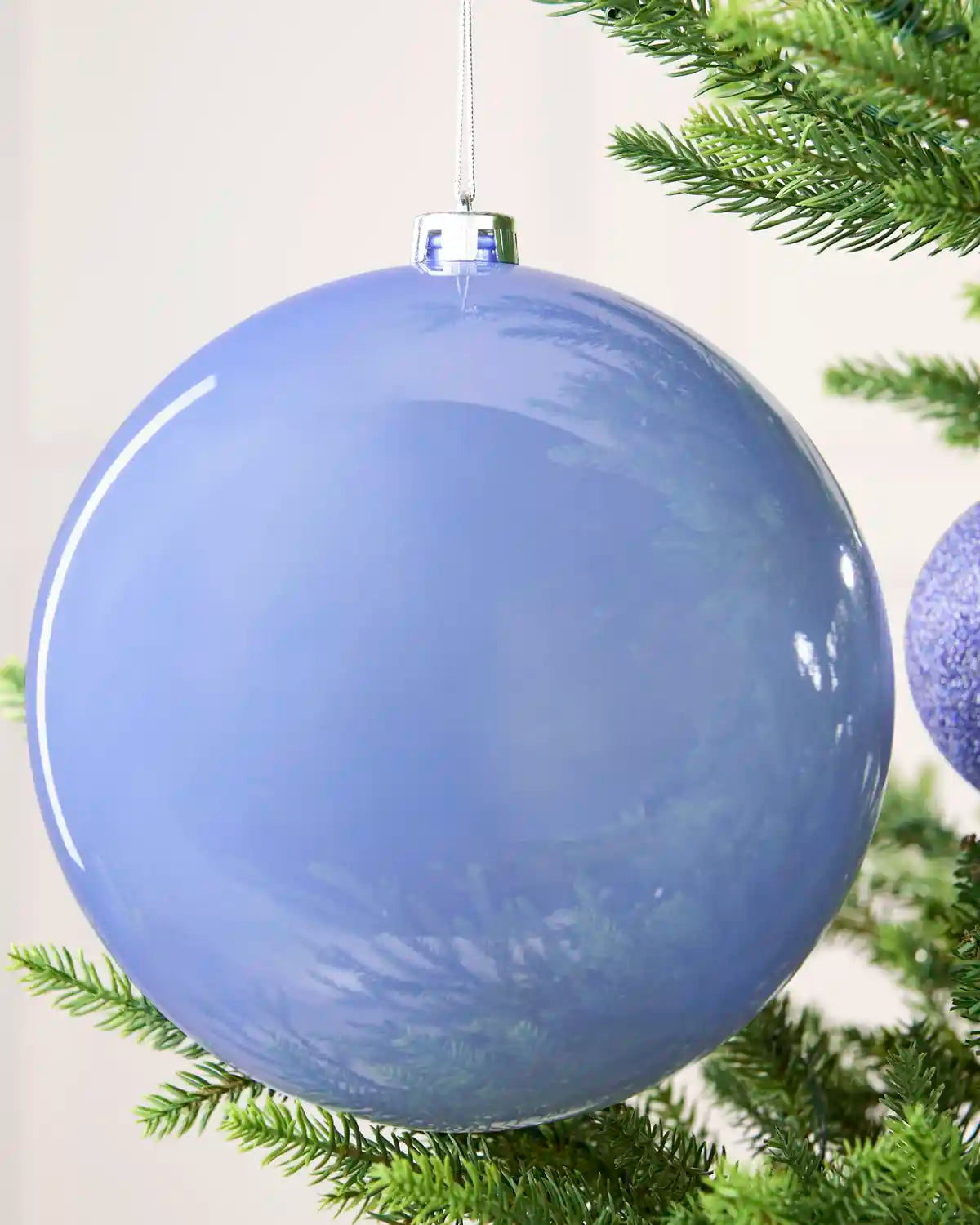 Oversized shiny ice blue bauble hanging on a Christmas tree against a cream background