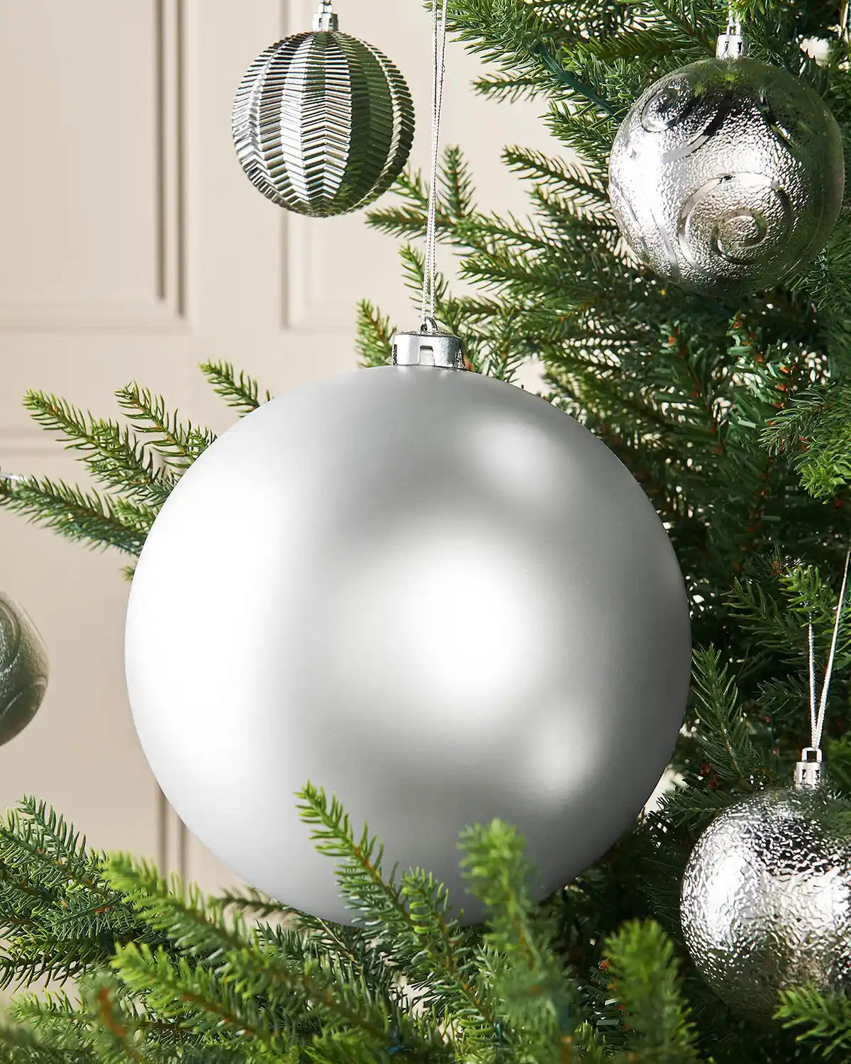 Oversized silver bauble on a Christmas tree branch with 4 smaller silver baubles in the background