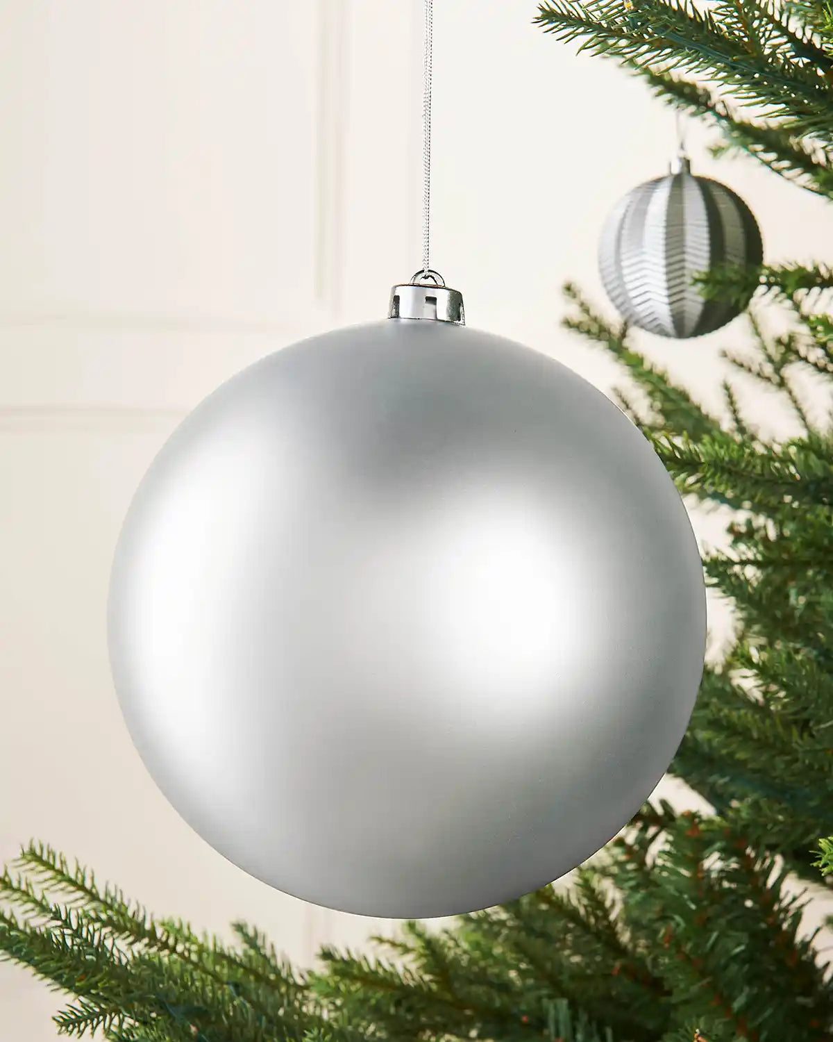 Oversized silver bauble on a Christmas tree branch with a smaller silver bauble in the background