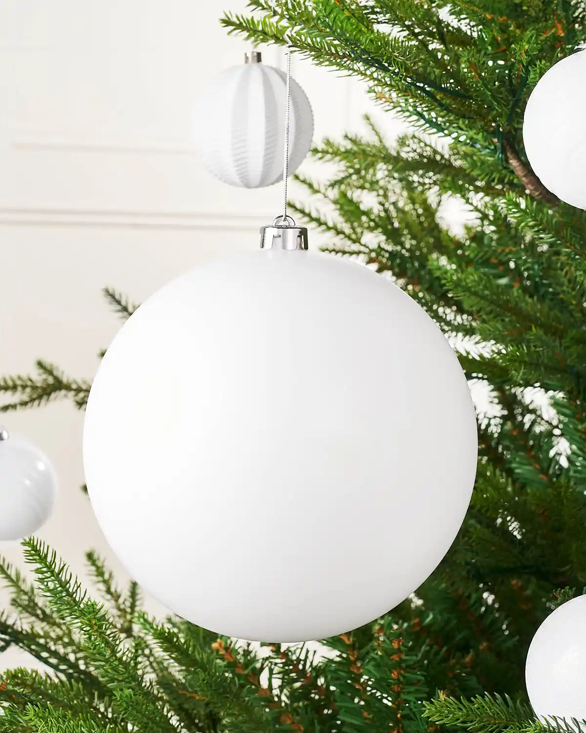 Oversized white matt bauble on a Christmas tree branch with 4 smaller white baubles in the background 