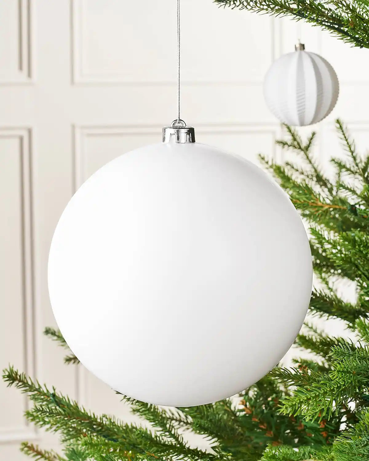 Oversized white matt bauble on a Christmas tree branch with a smaller white bauble in the background