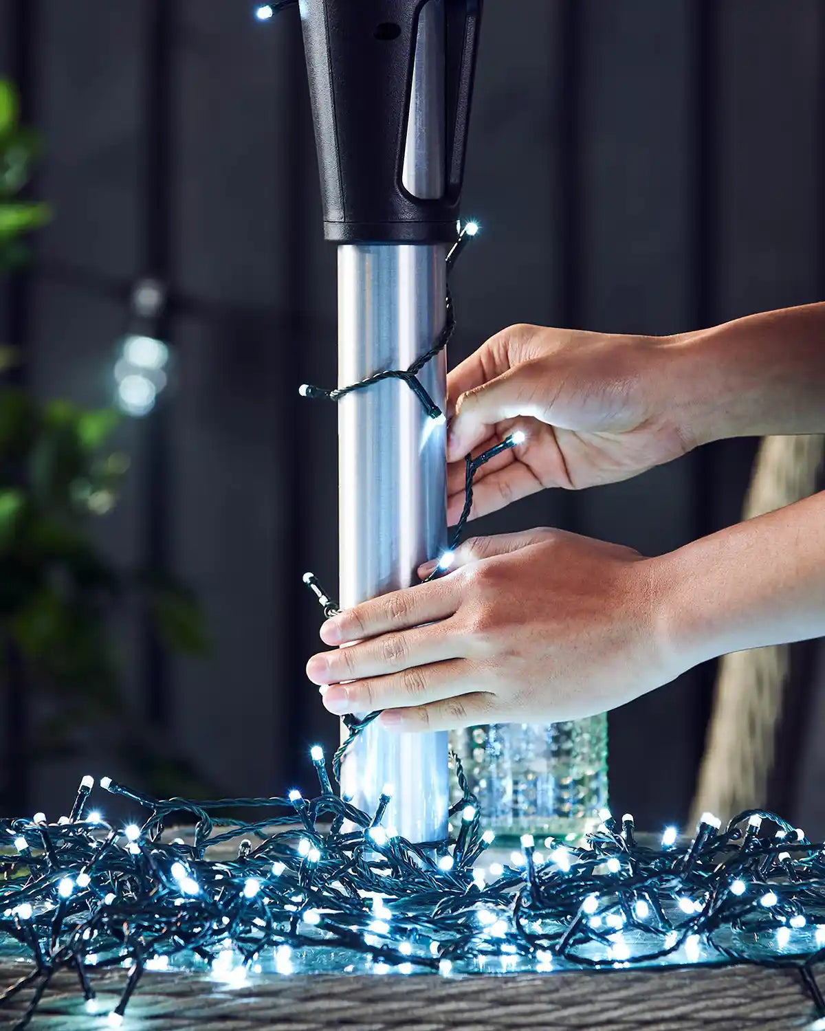 Person adjusting ice white string lights to an outdoor umbrella pole with a blurred background