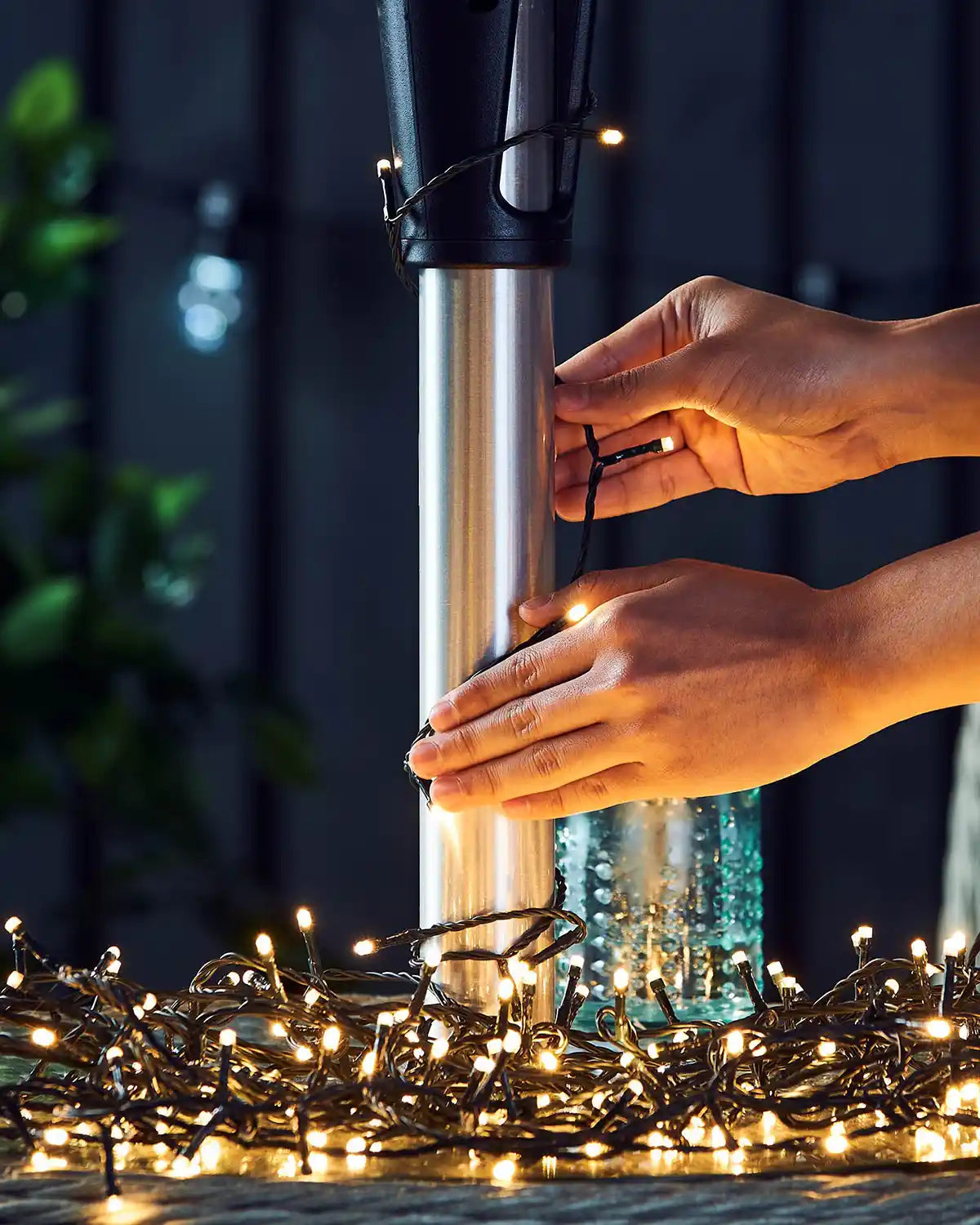 Person adjusting warm white string lights on an umbrella pole with a blurred background