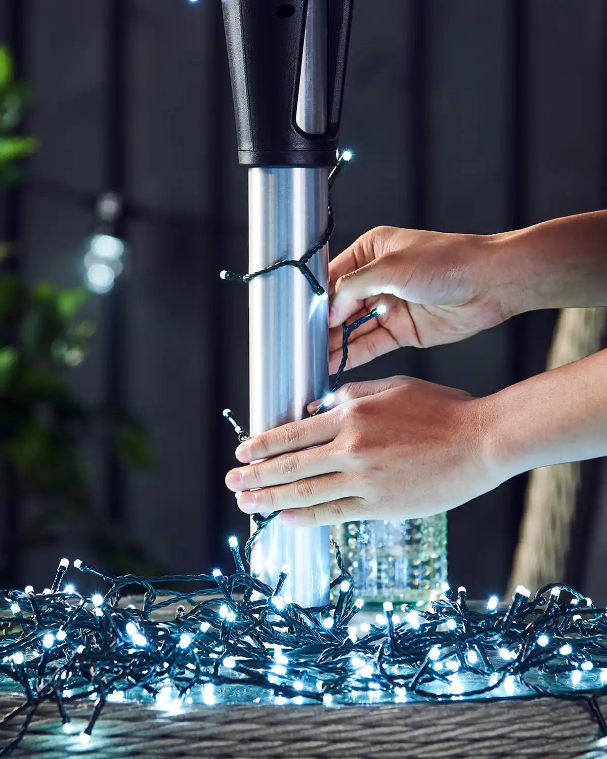 Person connecting ice white string lights to a metallic umbrella pole with a blurred background
