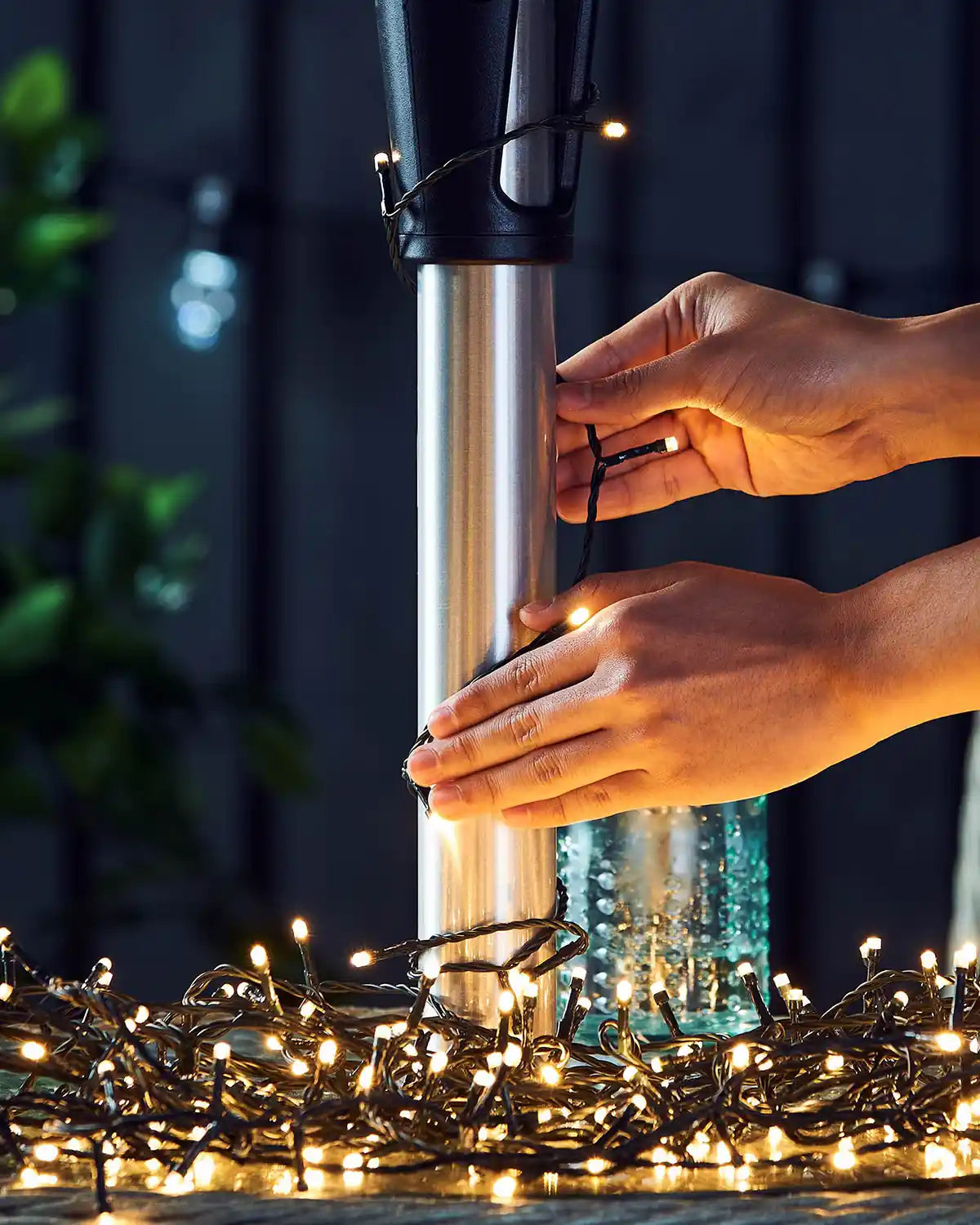 Person holding warm white string lights to a umbrella post with a dark background