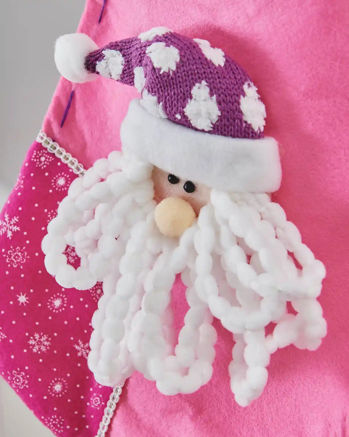Close up of 3D Santa Claus face and snowflake pattern on a pink Christmas Stocking.
