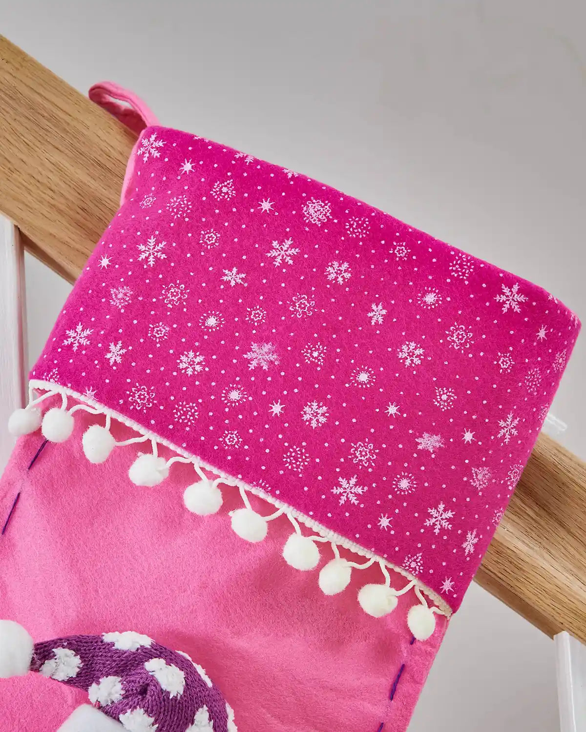 Close up of Snowflake pattern on a pink Christmas stocking on a wooden staircase banister. 
