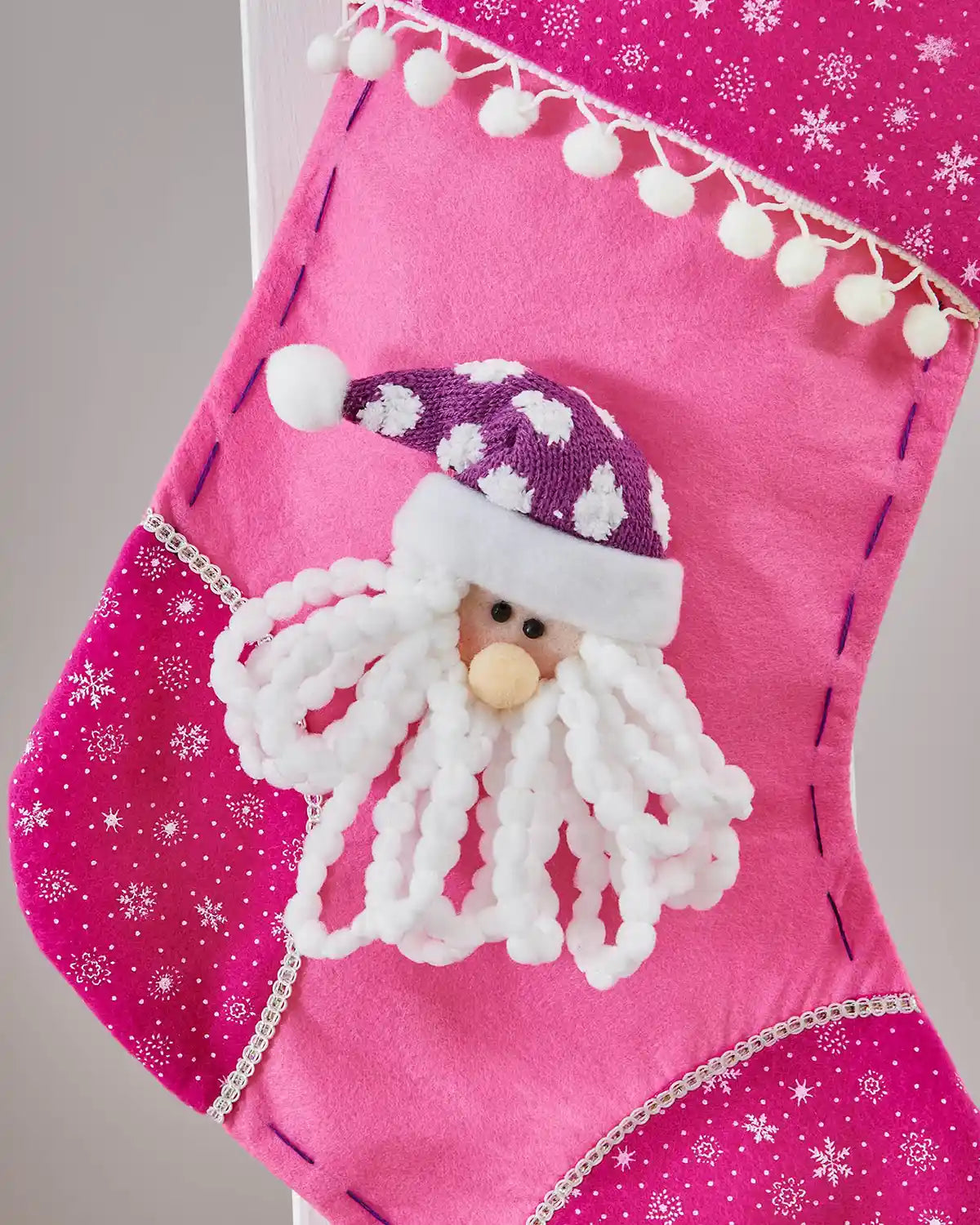 Pink Christmas stocking with 3D Santa Claus face and snowflake pattern on a wooden staircase banister with a Grey background. 
