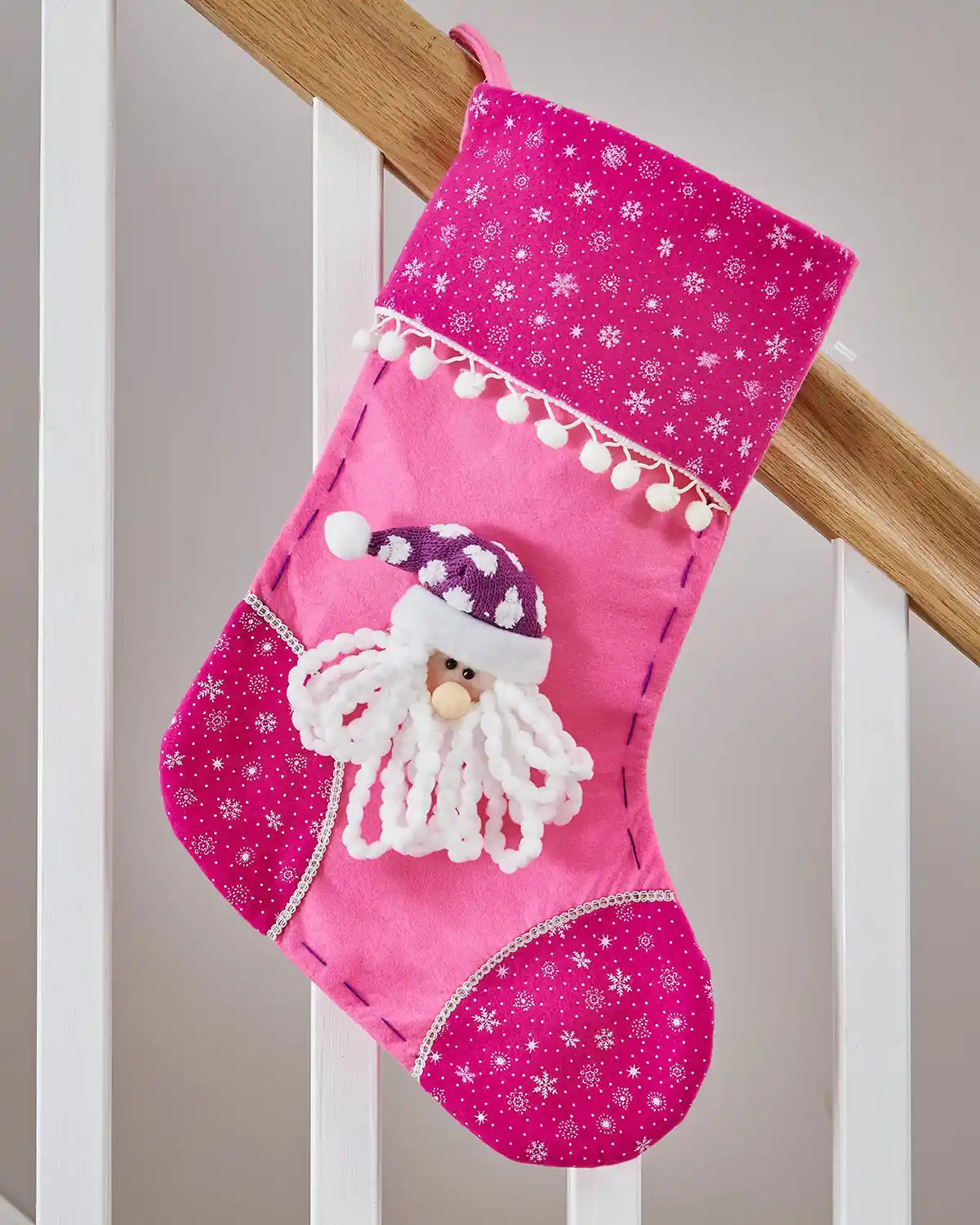 Pink Christmas stocking with 3D Santa Claus face and snowflake pattern on a wooden staircase banister.
