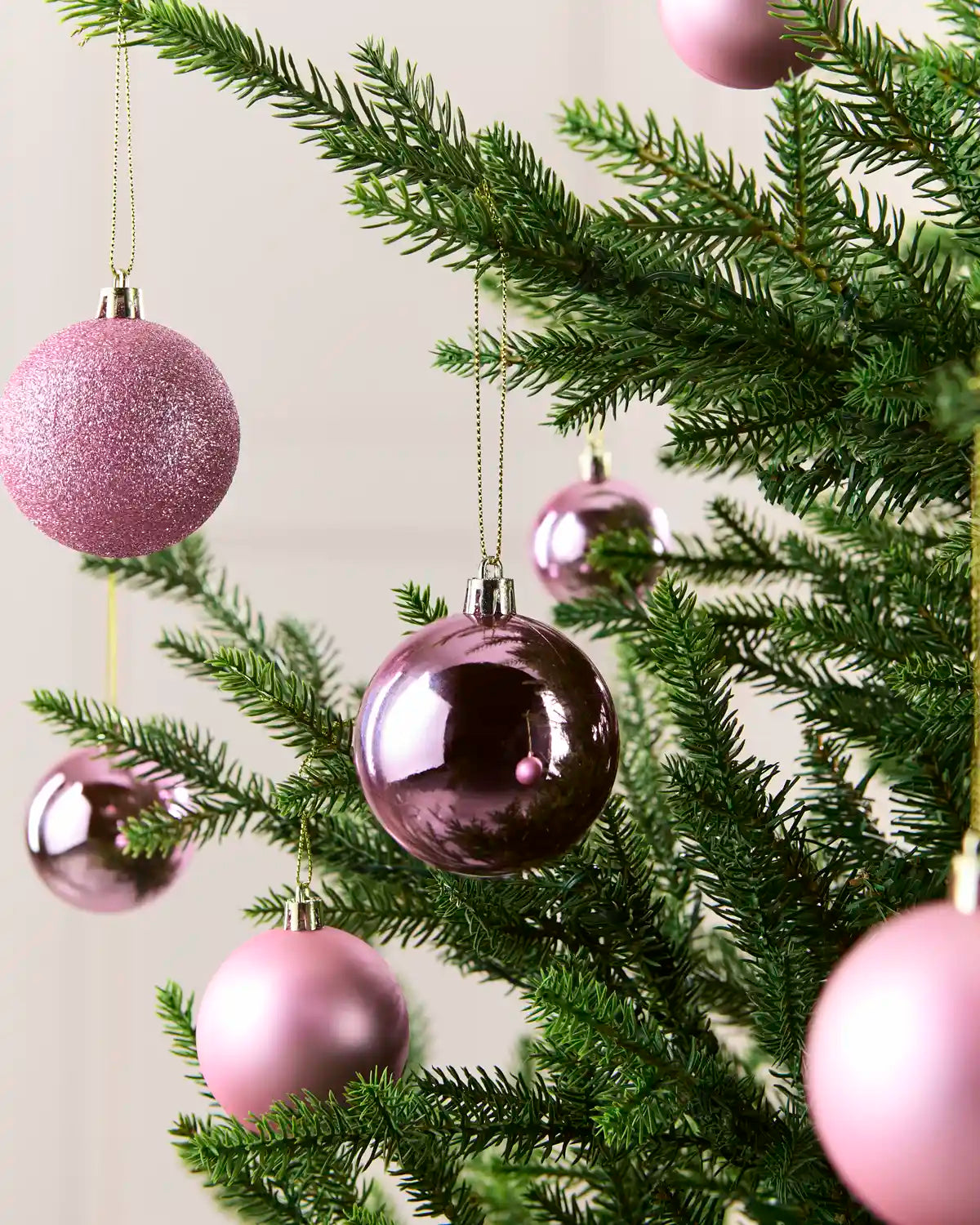 Pink Christmas tree baubles hanging on green pine branches against a soft light background.