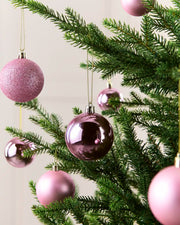 Pink Christmas tree baubles hanging on green pine branches against a soft light background.