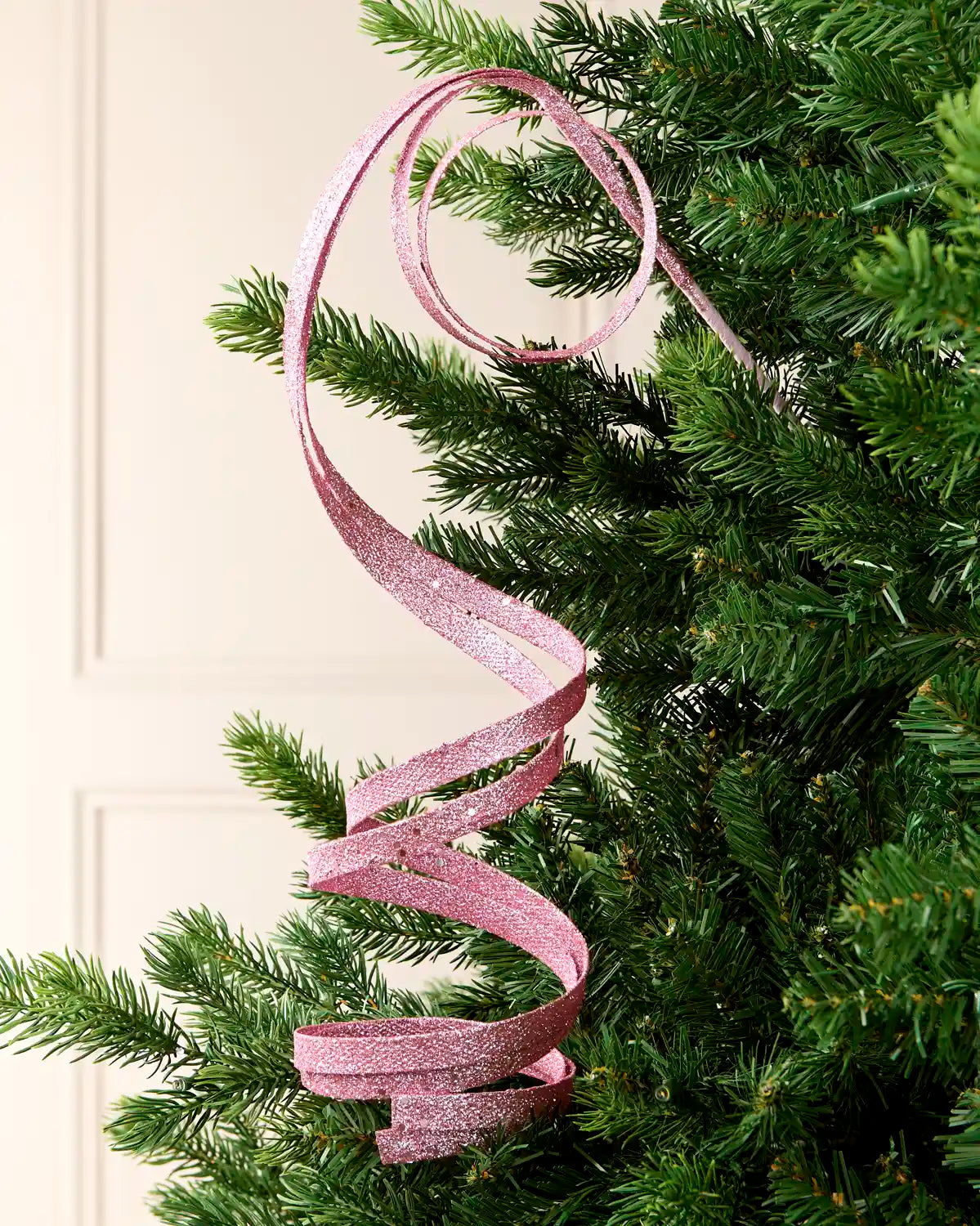 Pink Glitter Spiral Swirl Pick hanging from Christmas tree branch with cream background
