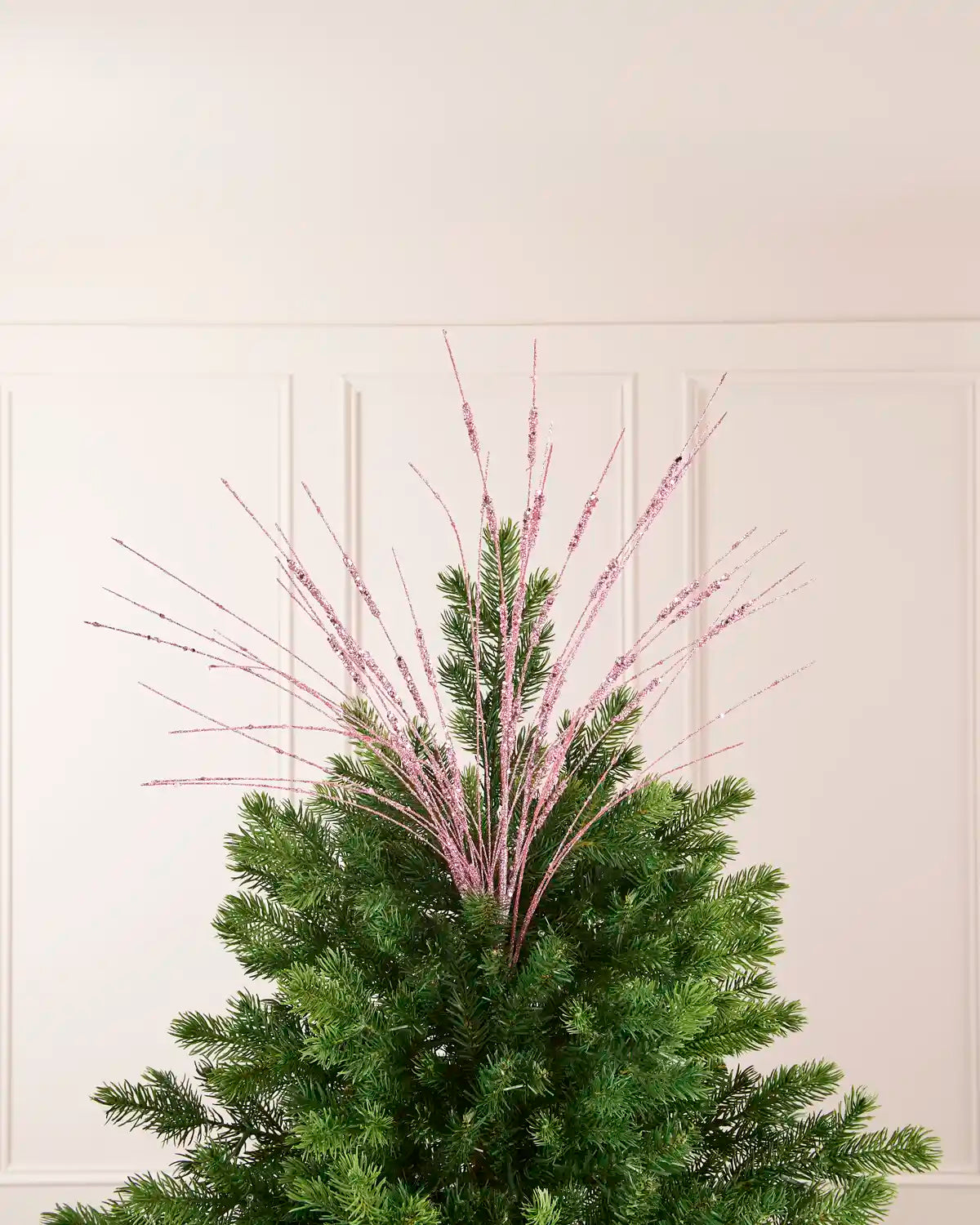 Pink Glitter Wispy Spray displayed at the top of a Christmas tree, with thin glitter-covered stems extending upward and outward
