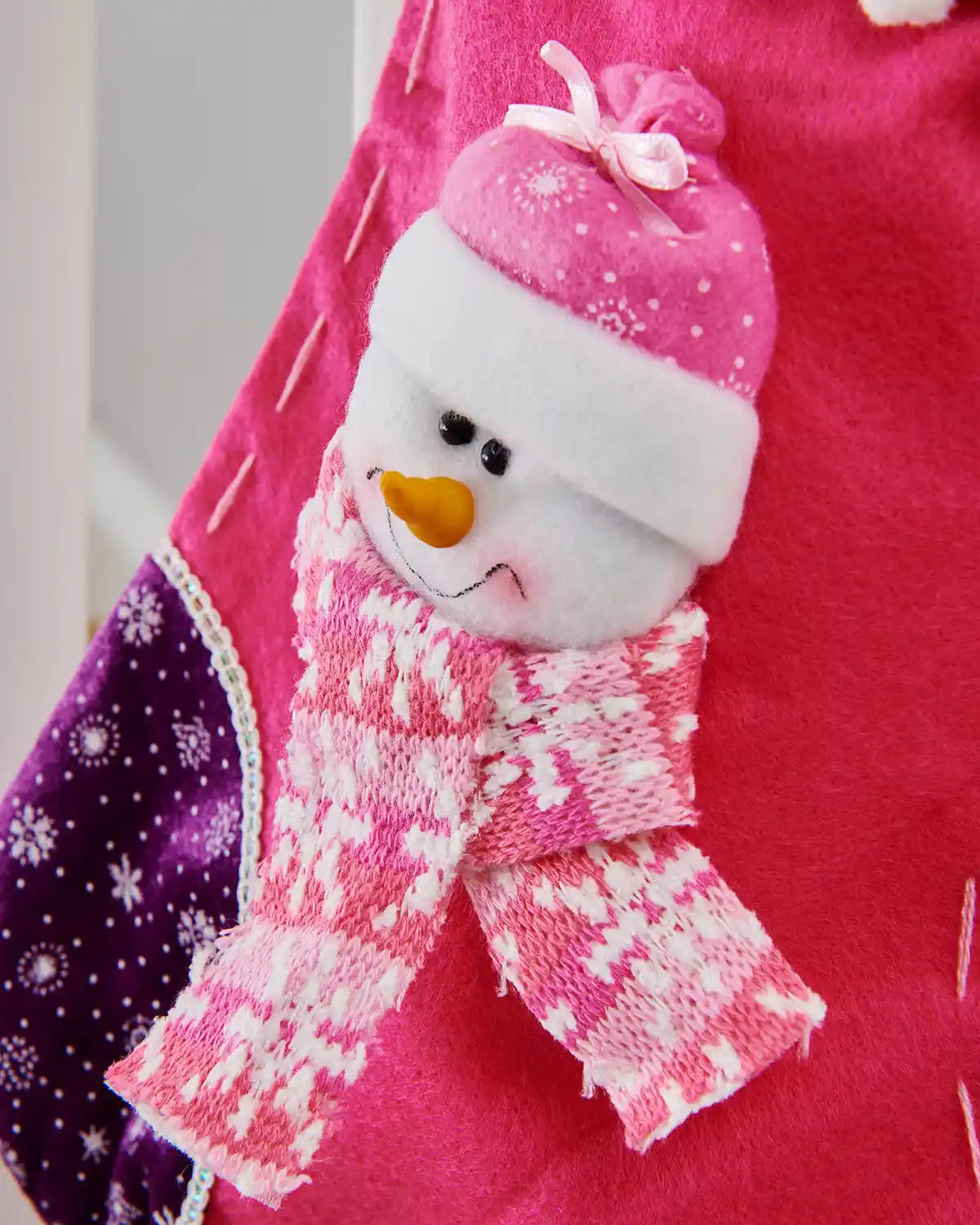 Close up of Pink and Purple Christmas stocking with 3D Snowman with Pink scarf and snowflake pattern with a Grey background. 
