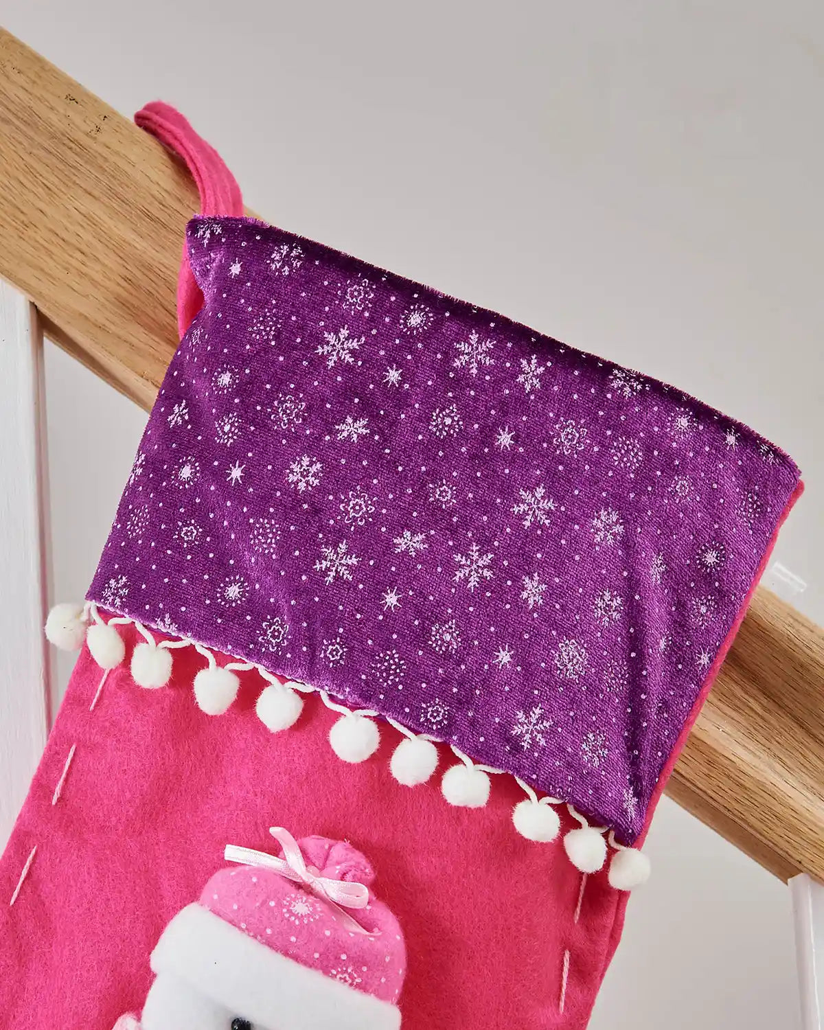 Close up of Purple Snowflake design  trim with White pom poms on a Pink and Purple Christmas stocking with 3D Snowman with Pink scarf. 
