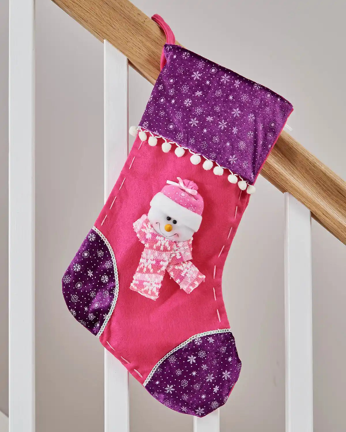 Pink and Purple Christmas stocking with 3D Snowman with Pink scarf and snowflake pattern with White pom poms hanging on a wooden staircase banister.