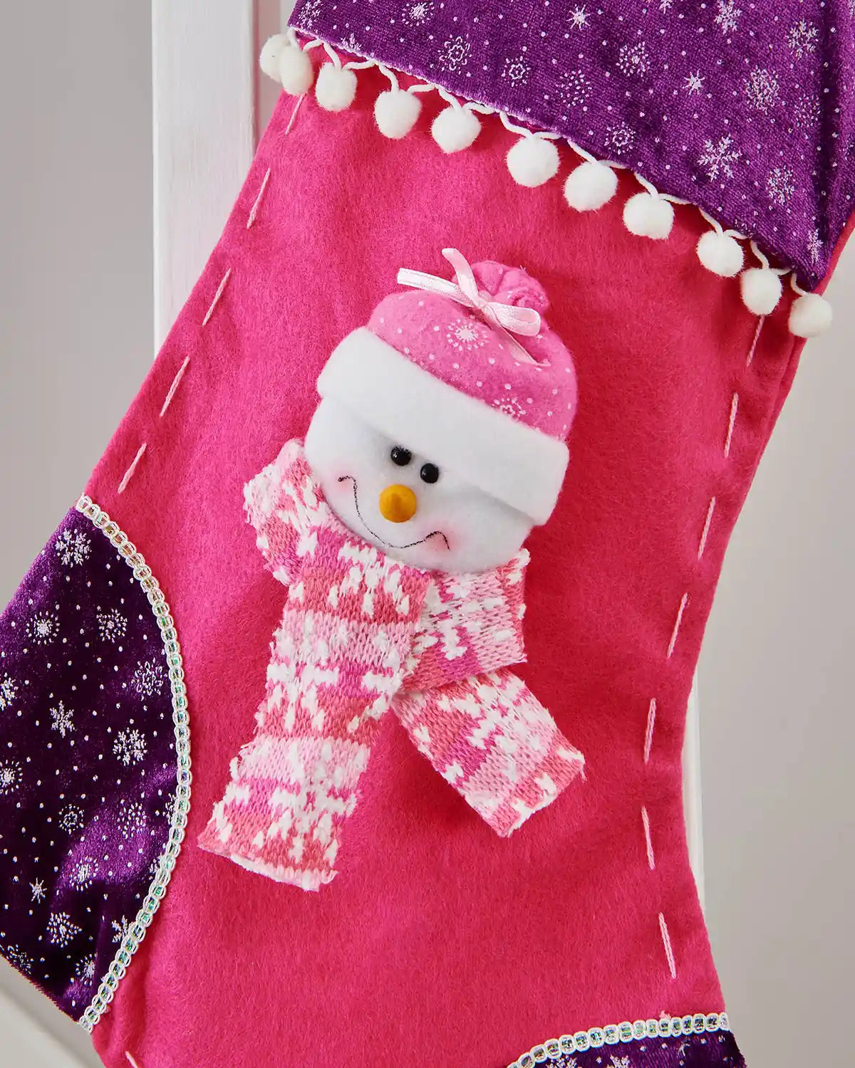 Close up of Pink and Purple Christmas stocking with 3D Snowman with Pink scarf and snowflake pattern on a wooden staircase banister and a Grey background. 

