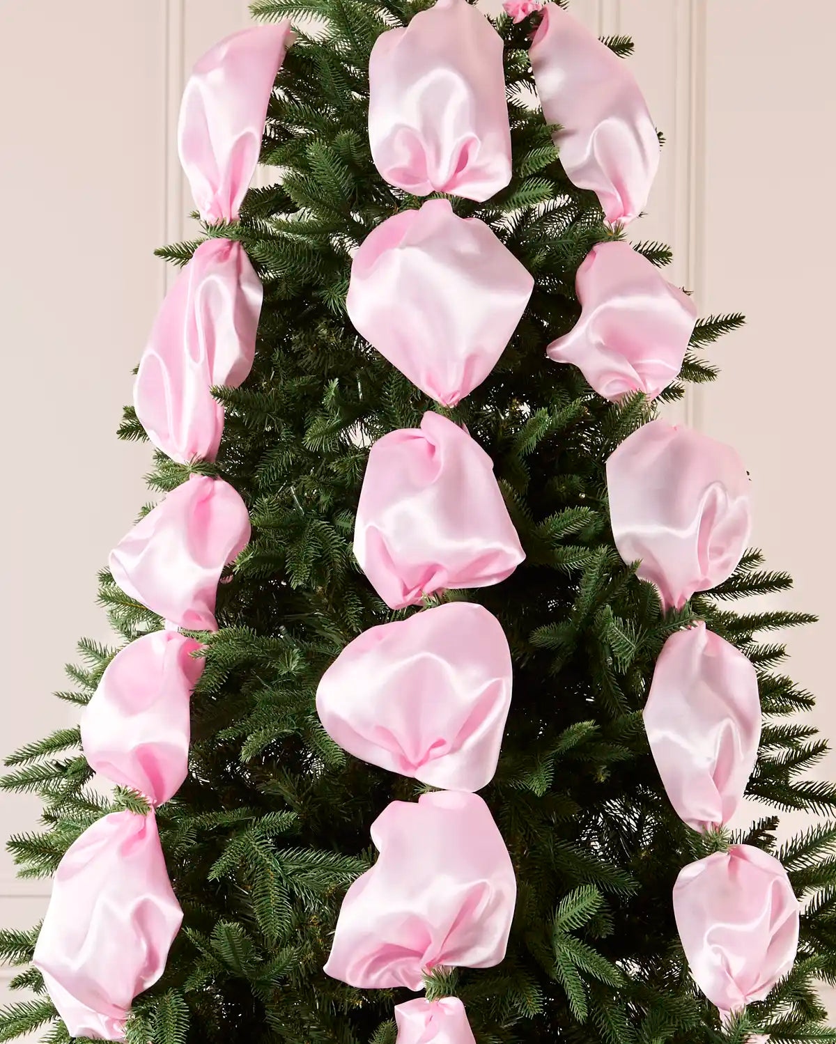 Pink satin ribbon draped and arranged on a green Christmas tree.