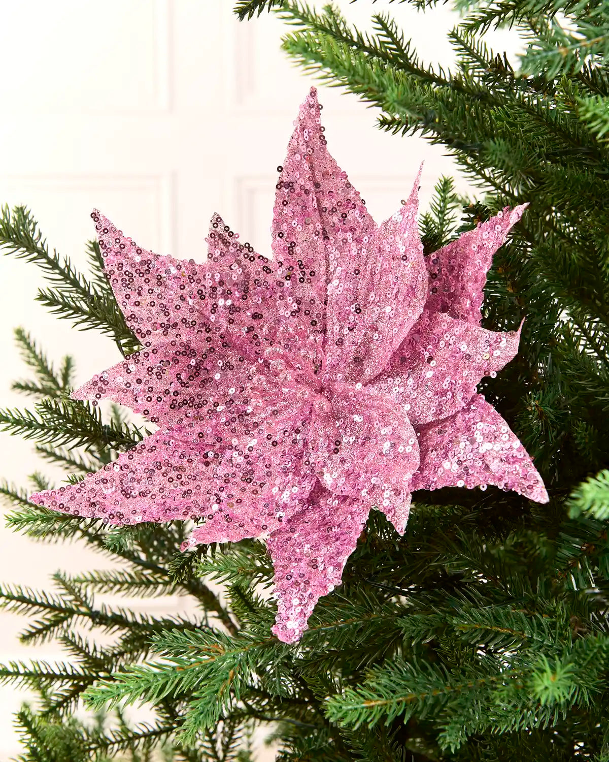 Pink sequin poinsettia on a Christmas tree against a cream background