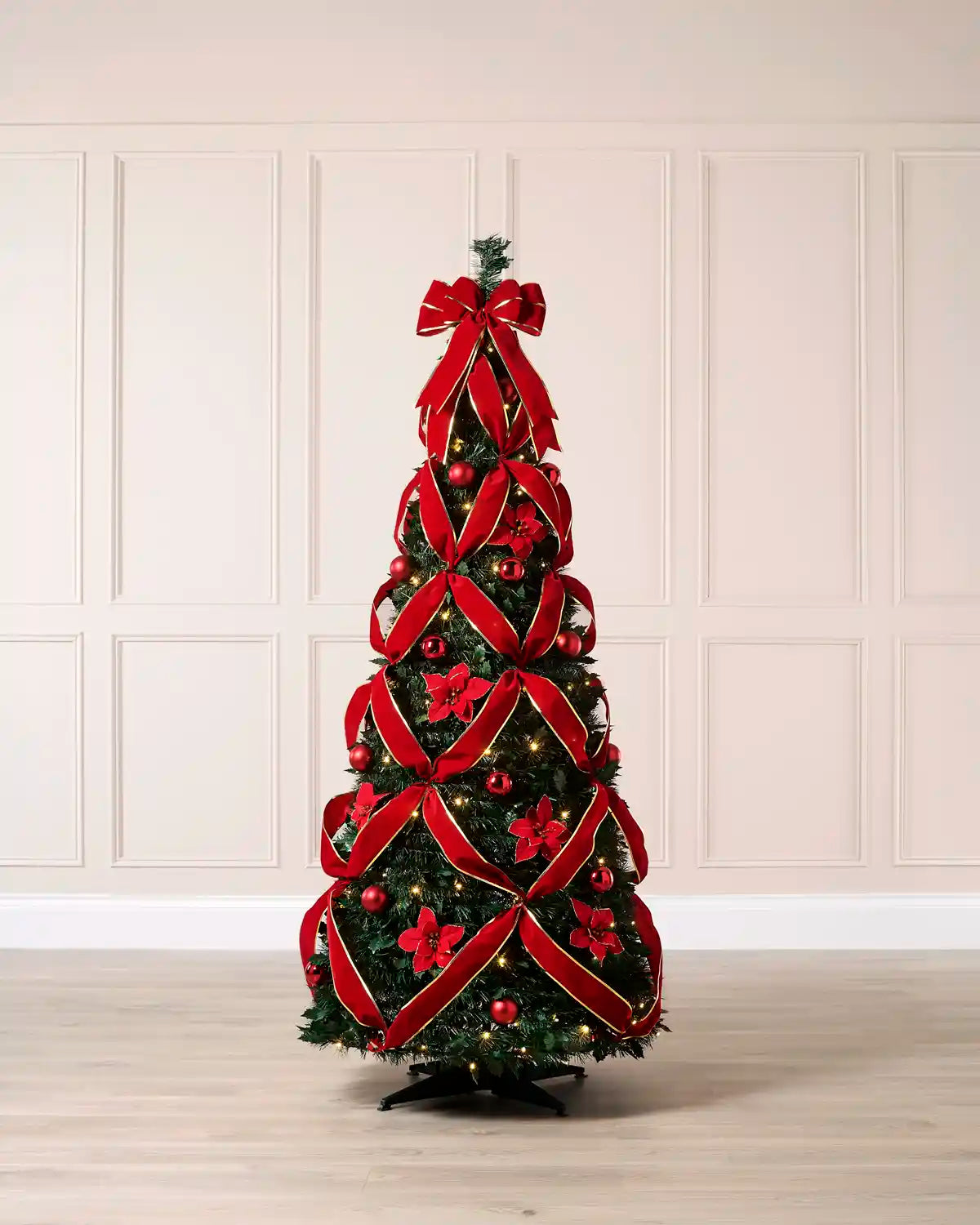 Pop up red poinsettia and ribbon Christmas tree with a red bow at the top n a wooden floor against a light background