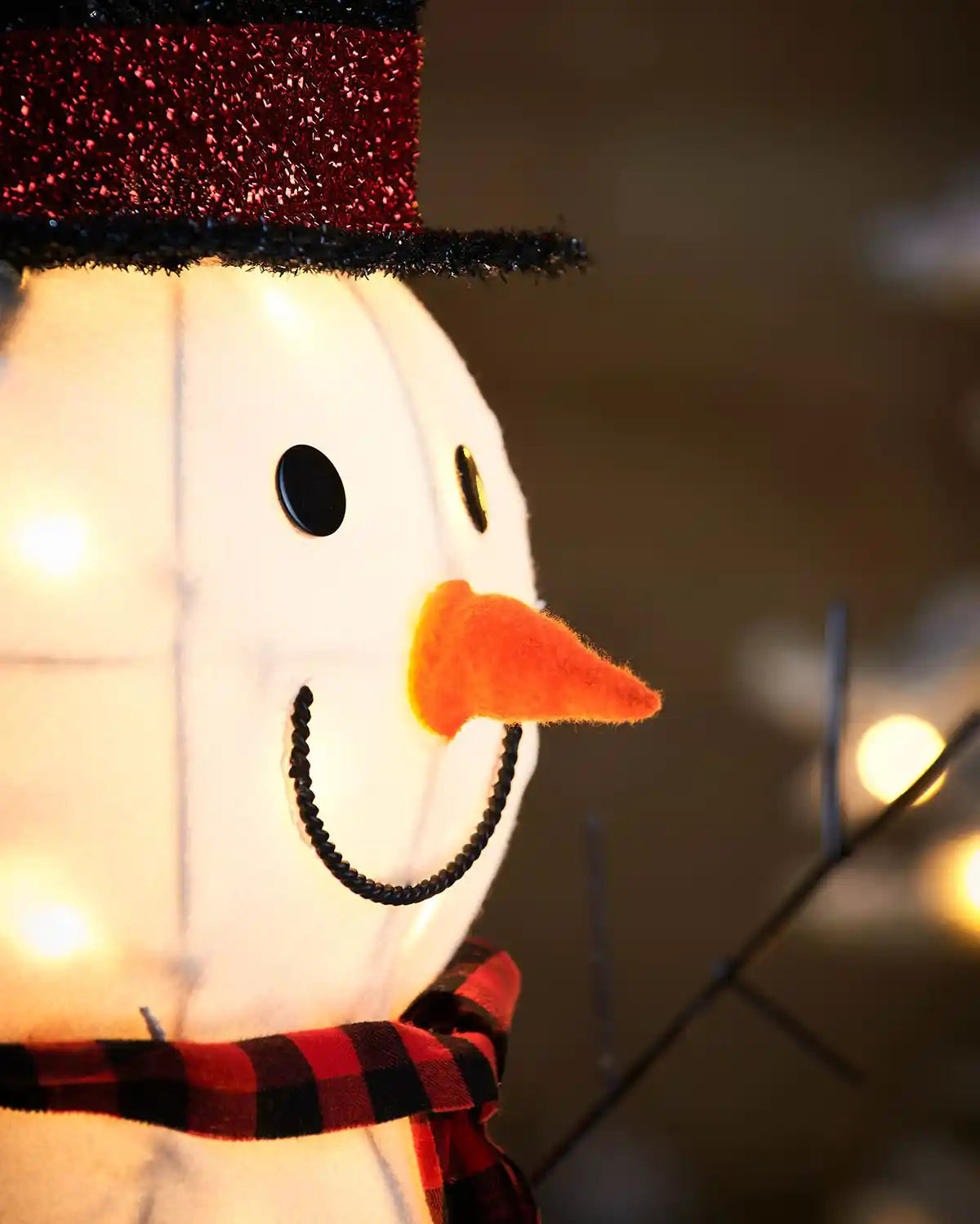 Close up of Snowman's face with carrot nose and black and red scarf Pre-Lit 3D Snowman, Silhouette, 95 cm with lights in background