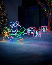 Pre-Lit Animated Flying Santa, Silhouette, 190 cm in a garden with trees wrapped in Christmas lights and snowy floor
