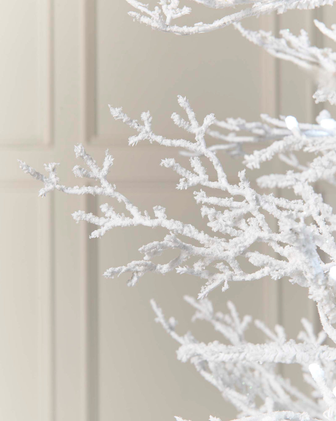 Minimalistic pre-lit white Arctic Ice Twig Christmas tree with snow-flocked PE/PVC branches, glowing with bright white LED lights against a neutral wall—crafted for easy setup and timeless winter charm.
