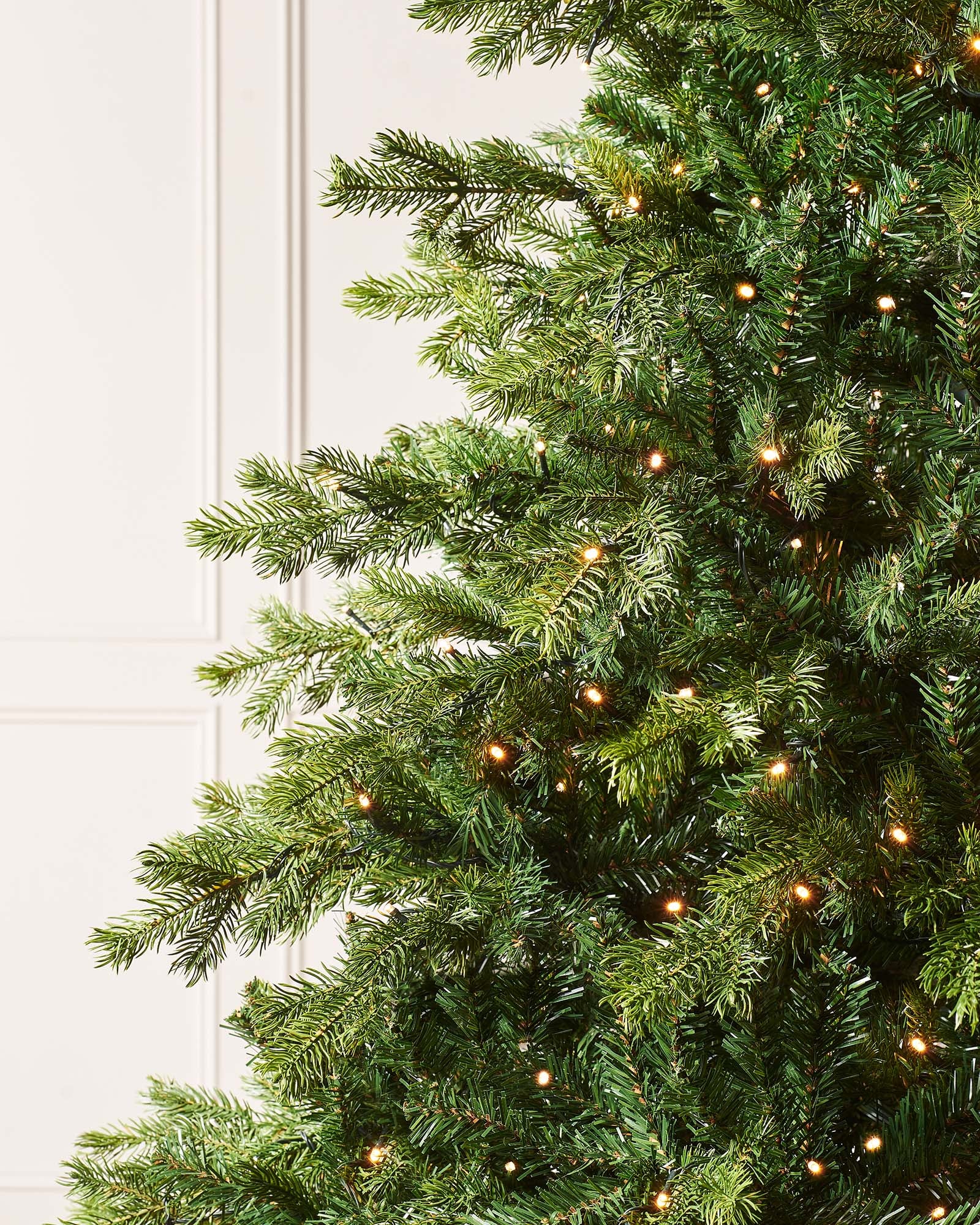 Pre-lit Balsam Fir Christmas tree with lush PE and PVC tips, adorned with warm white LED lights, displayed against a white wall—realistic, full-bodied, and perfect for creating a warm, elegant festive ambiance indoors or out.