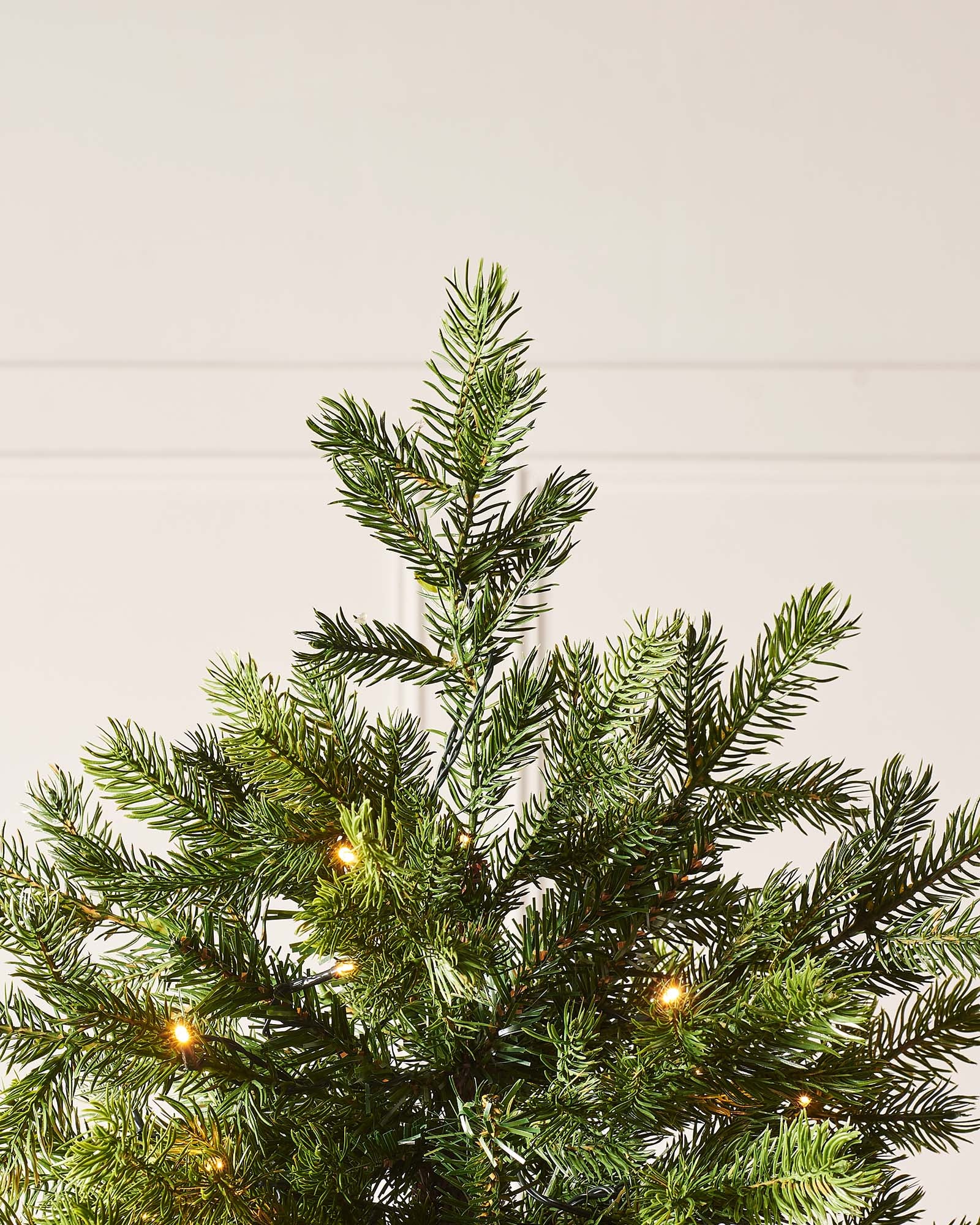 Pre-lit Balsam Fir Christmas tree with lush PE and PVC tips, adorned with warm white LED lights, displayed against a white wall—realistic, full-bodied, and perfect for creating a warm, elegant festive ambiance indoors or out.