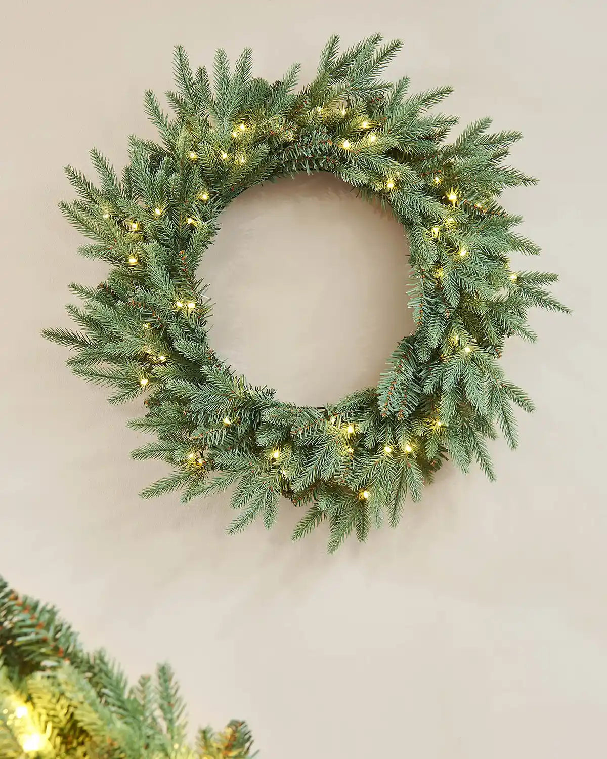 Pre-Lit Blue Mixed Pine Wreath, 60 cm with warm white lights on a cream wall