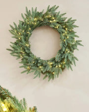 Pre-Lit Blue Mixed Pine Wreath, 60 cm with warm white lights on a cream wall