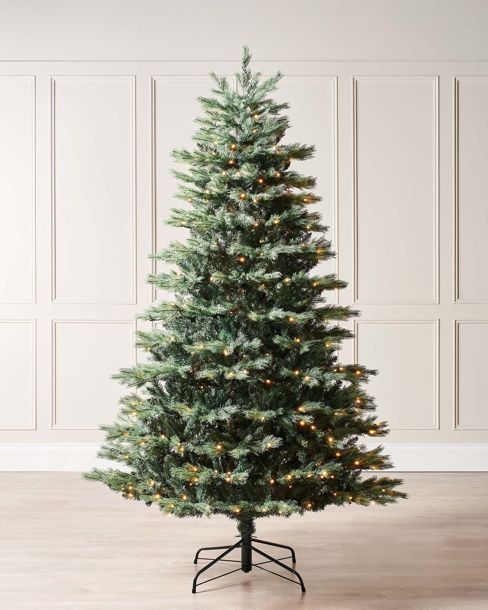 Pre-lit Colorado Blue Spruce Christmas tree with lifelike blue PE/PVC branches and built-in warm white LED lights, displayed indoors against a white wall—realistic texture, soft glow, and effortless festive elegance.