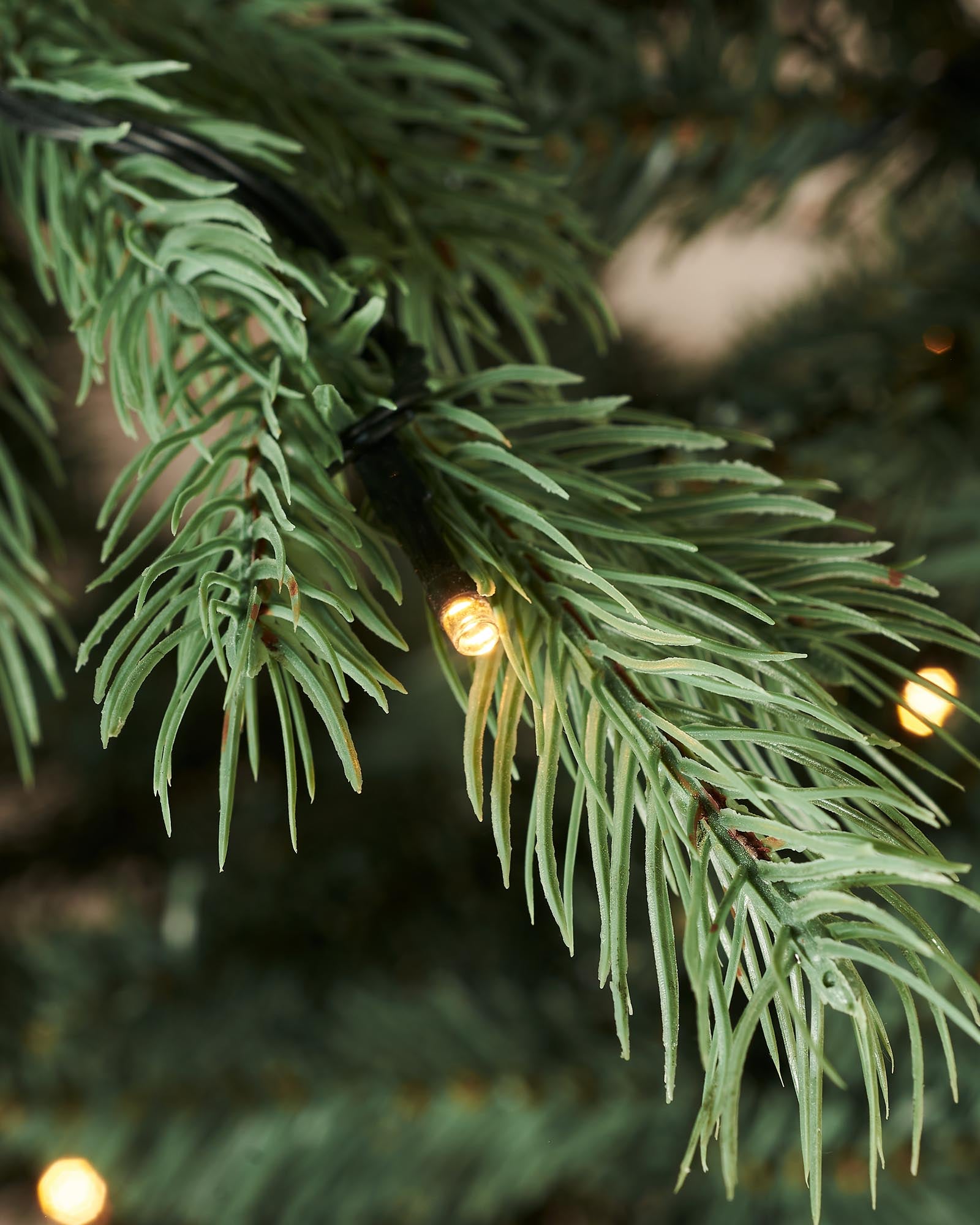 Pre-lit Colorado Blue Spruce Christmas tree with lifelike blue PE/PVC branches and built-in warm white LED lights, displayed indoors against a white wall—realistic texture, soft glow, and effortless festive elegance.
