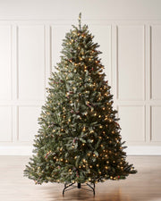 A pre-lit decorated Christmas tree with snow flocked branches, warm white LEDs, and adorned with berries and pinecones, displayed indoors. Pre-lit decorated snow flocked Christmas tree with warm white LED lights, natural-looking berries and pinecones, and 8-function lighting settings—suitable for indoor and outdoor use, featuring a full snowy design for a winter wonderland effect.