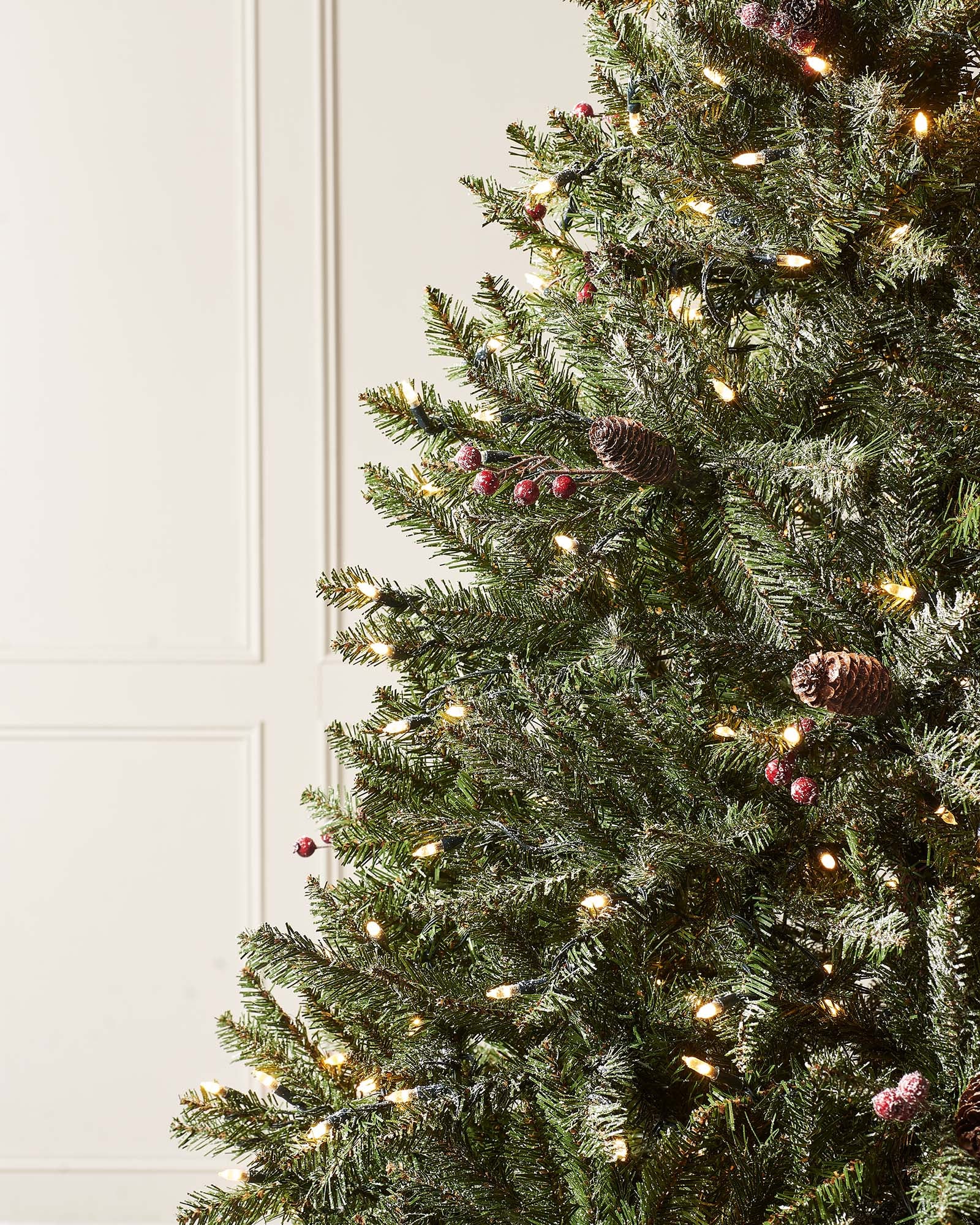 A pre-lit decorated Christmas tree with snow flocked branches, warm white LEDs, and adorned with berries and pinecones, displayed indoors. Pre-lit decorated snow flocked Christmas tree with warm white LED lights, natural-looking berries and pinecones, and 8-function lighting settings—suitable for indoor and outdoor use, featuring a full snowy design for a winter wonderland effect.