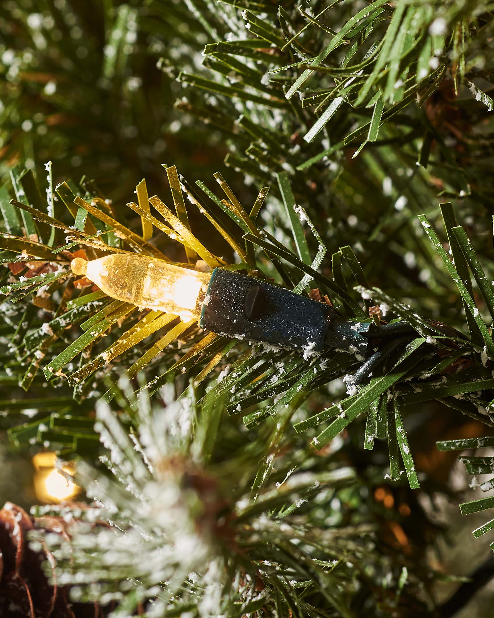 A pre-lit decorated Christmas tree with snow flocked branches, warm white LEDs, and adorned with berries and pinecones, displayed indoors. Pre-lit decorated snow flocked Christmas tree with warm white LED lights, natural-looking berries and pinecones, and 8-function lighting settings—suitable for indoor and outdoor use, featuring a full snowy design for a winter wonderland effect.