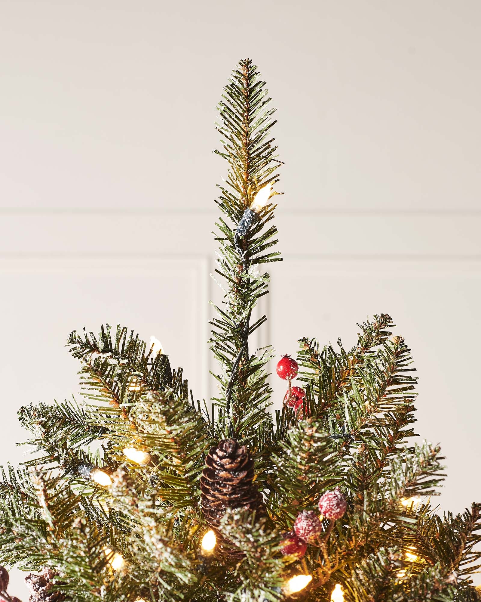 A pre-lit decorated Christmas tree with snow flocked branches, warm white LEDs, and adorned with berries and pinecones, displayed indoors. Pre-lit decorated snow flocked Christmas tree with warm white LED lights, natural-looking berries and pinecones, and 8-function lighting settings—suitable for indoor and outdoor use, featuring a full snowy design for a winter wonderland effect.