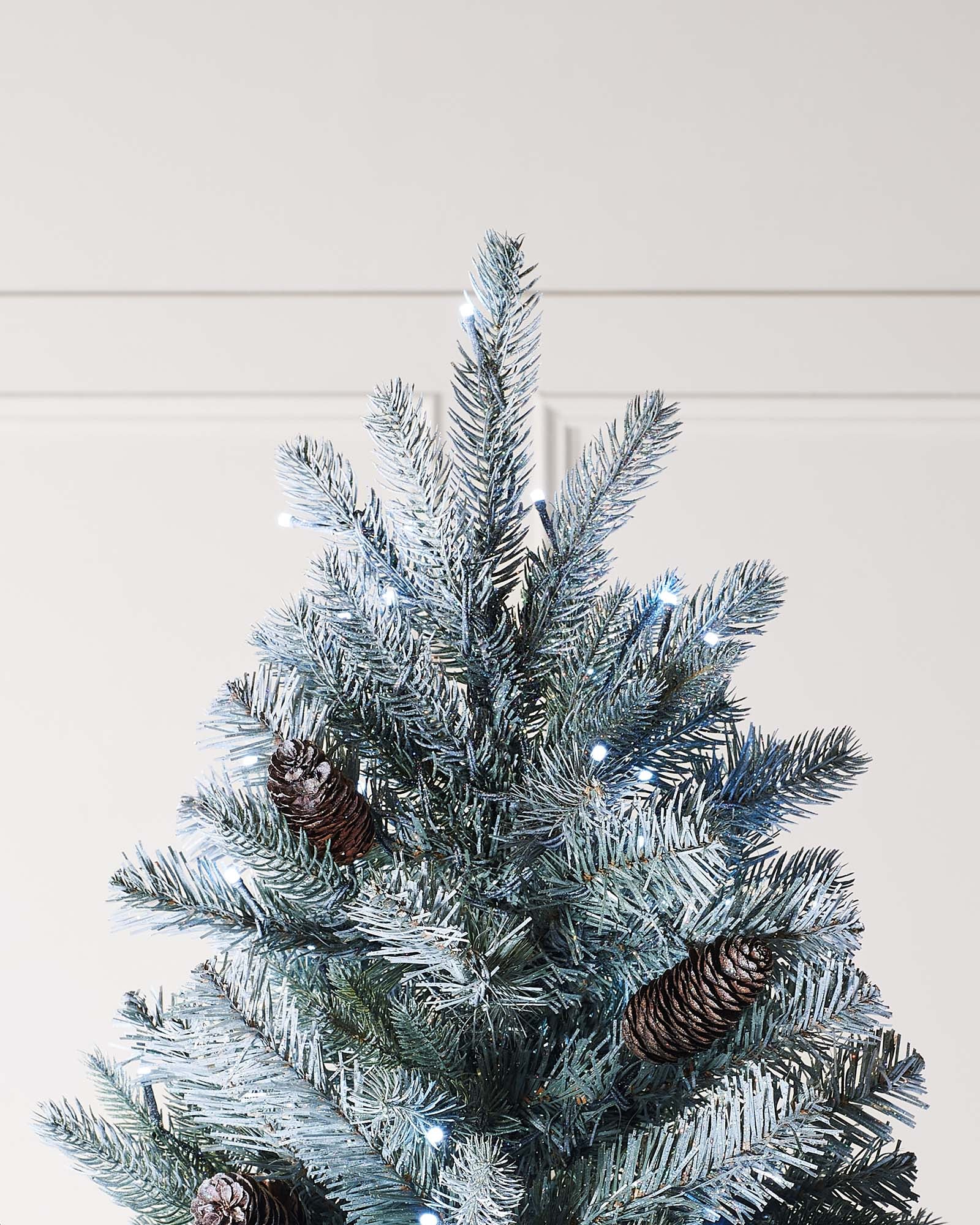 Pre-lit Elegant Spruce artificial Christmas tree with mixed PE and PVC branches, realistic pinecones, glitter finish, and bright white LED lights with multi-function settings, displayed in an indoor setting.