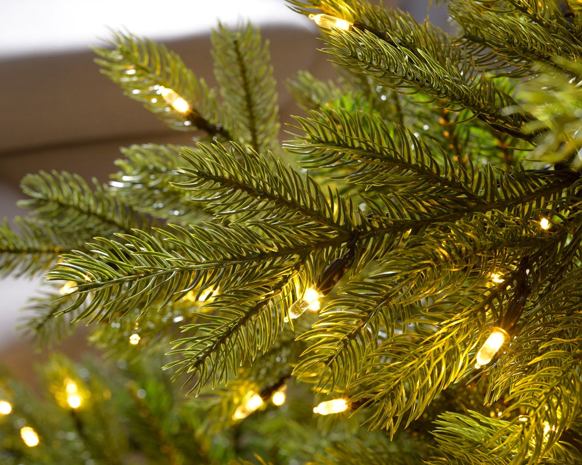 7-foot pre-lit Empress Pine Christmas tree with green pine branches, 500 warm white LED lights, natural-looking berries and pinecones, featuring 8 lighting functions, displayed indoors with presents underneath.