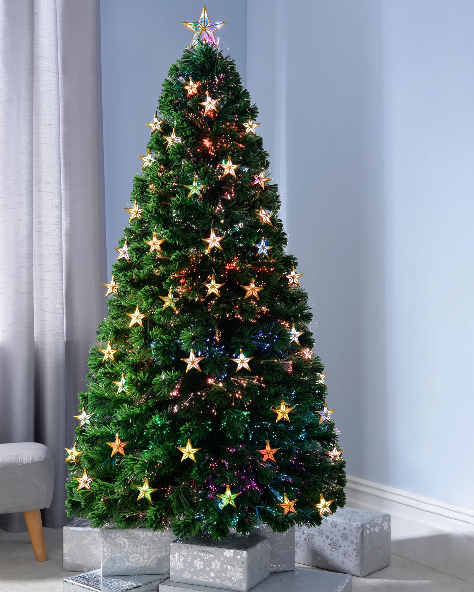 6 ft pre-lit fibre optic Christmas tree with 220 multi-colour fibre optic tips, 50 LED star decorations, and a bright LED star topper. Displayed indoors with warm, dynamic lighting and a 1.8 m lead wire.